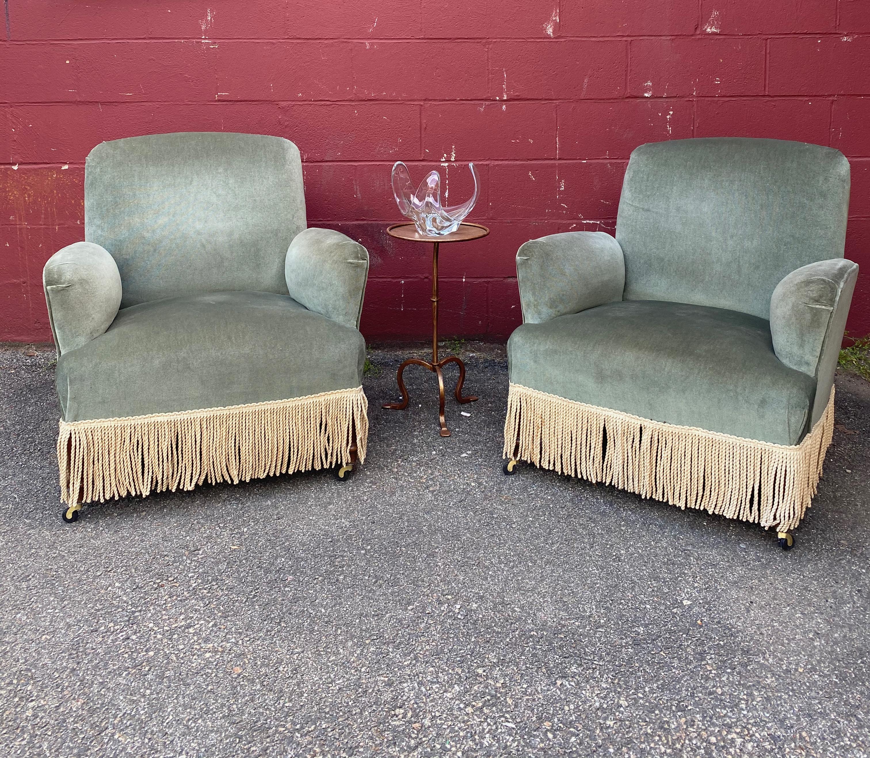 An unusual pair of French Napoleon III armchairs that are upholstered in green velvet with contrasting bullion fringe. The arms are made to appear to be detachable although they are attached. The fabric is not new and shows signs of use. We have
