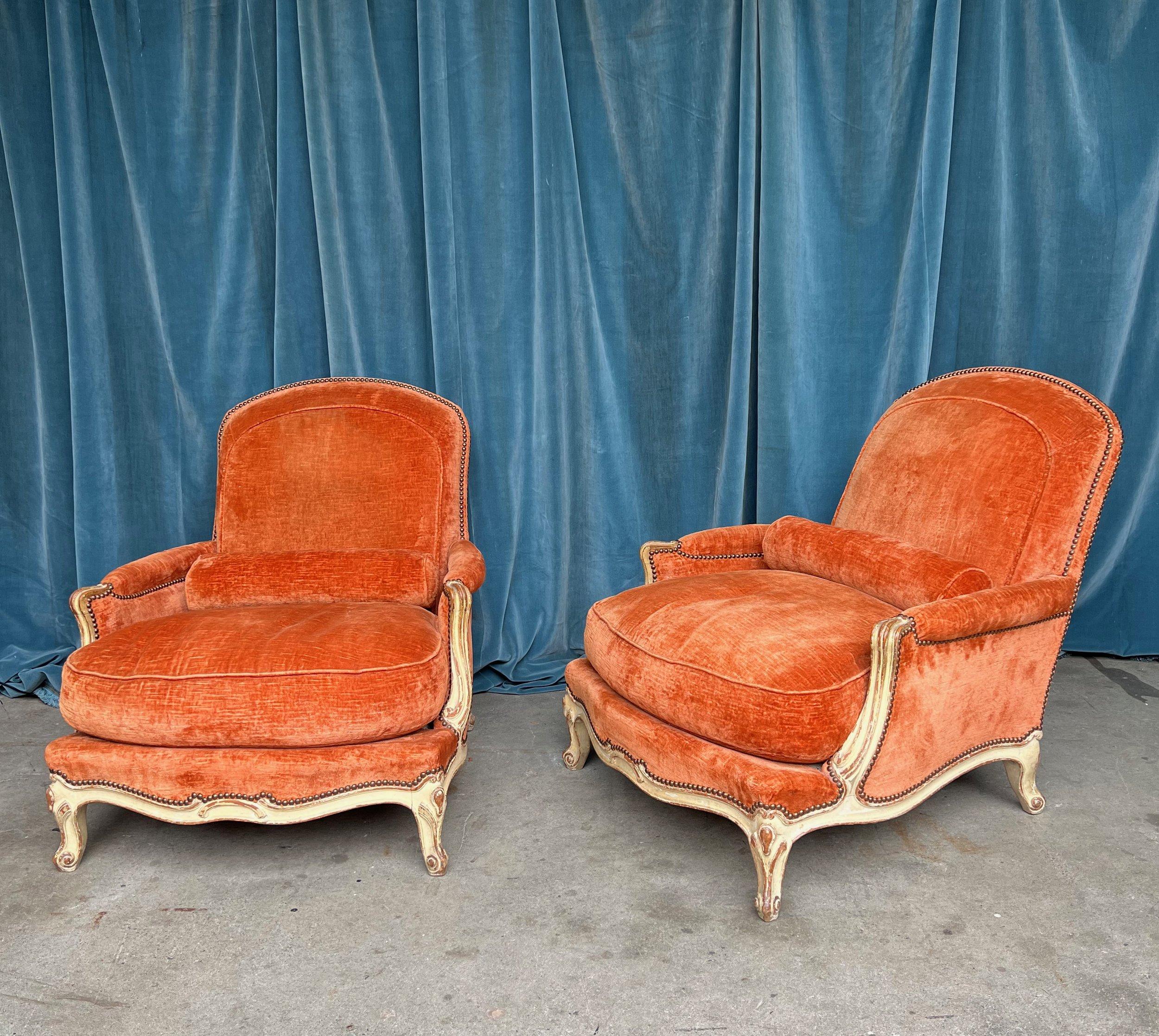 A large pair of French 19th century armchairs upholstered in crushed orange velvet with cabriole legs in the Louis XV style. Immerse yourself in the opulence of French design with this exquisite pair of large scale vintage armchairs, embodying the