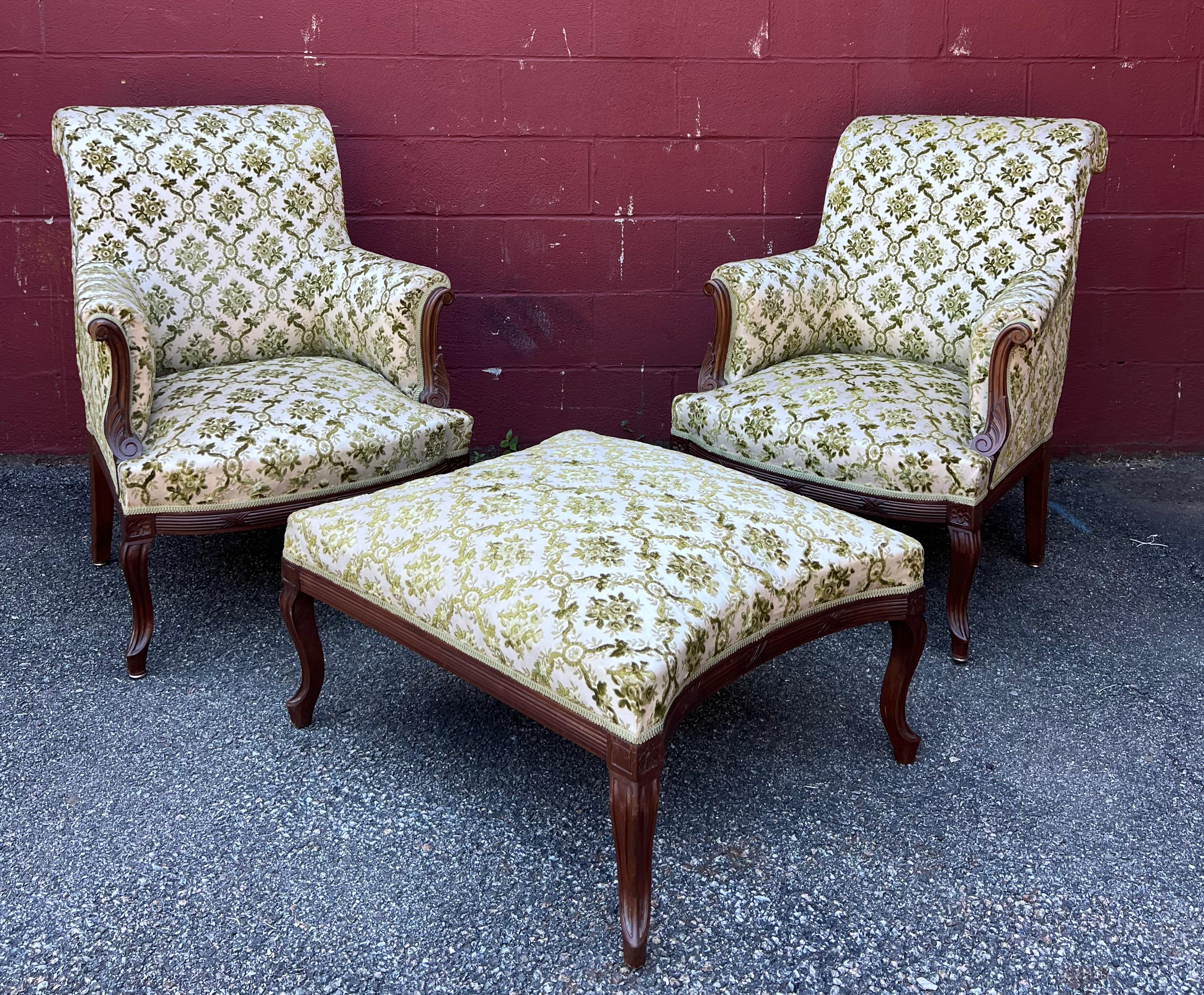 An exquisite pair of French 1920s armchairs with matching ottoman. This stunning set will be sure to add a breathtaking vintage touch to your interior. These finely crafted pieces feature elaborately carved wooden frames that are stained in an