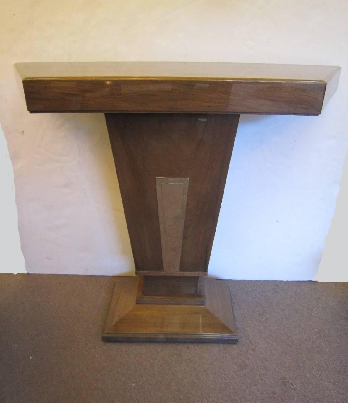A French moderne grained walnut, gloss lacquered console of cubist design, displaying a tapered angular shaped base with geometric nickeled bronze stepped accent detailing which rests on a rectangular molded plinth.
Note: The front width is 26