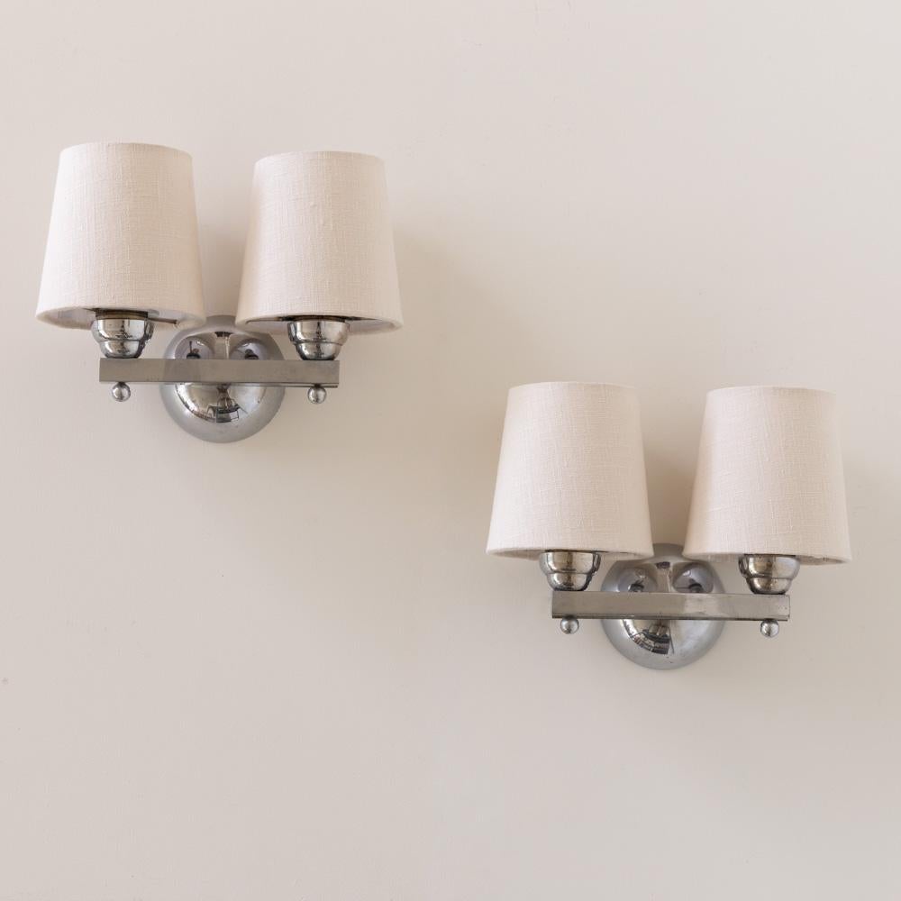 Incredible pair of petite two arm sconces from France, 1930's. Great Art Deco style in chrome with two arms on straight chrome bar with ball detail. Newly rewired with new tapered linen shades. Takes an E12 base bulb, 25 W or higher using LED. 