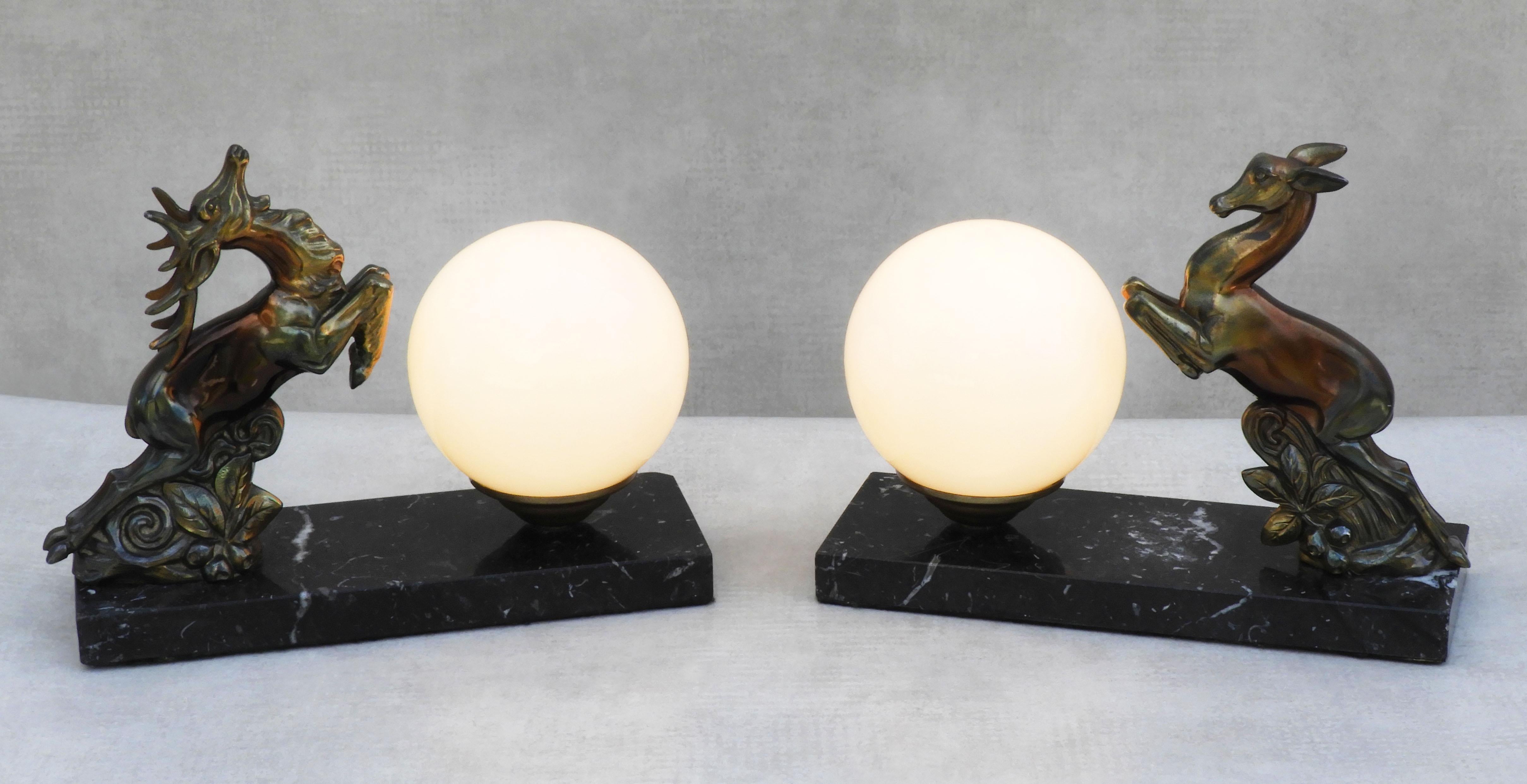 Charming pair of Art Deco 'Deer' table lamps or night-light sculptures from 1930s France. A couple of male and female deer sculptures in iridescent bronzed spelter on marble plinths posed to leap over the opaline glass 'full moon' shades. 
In good