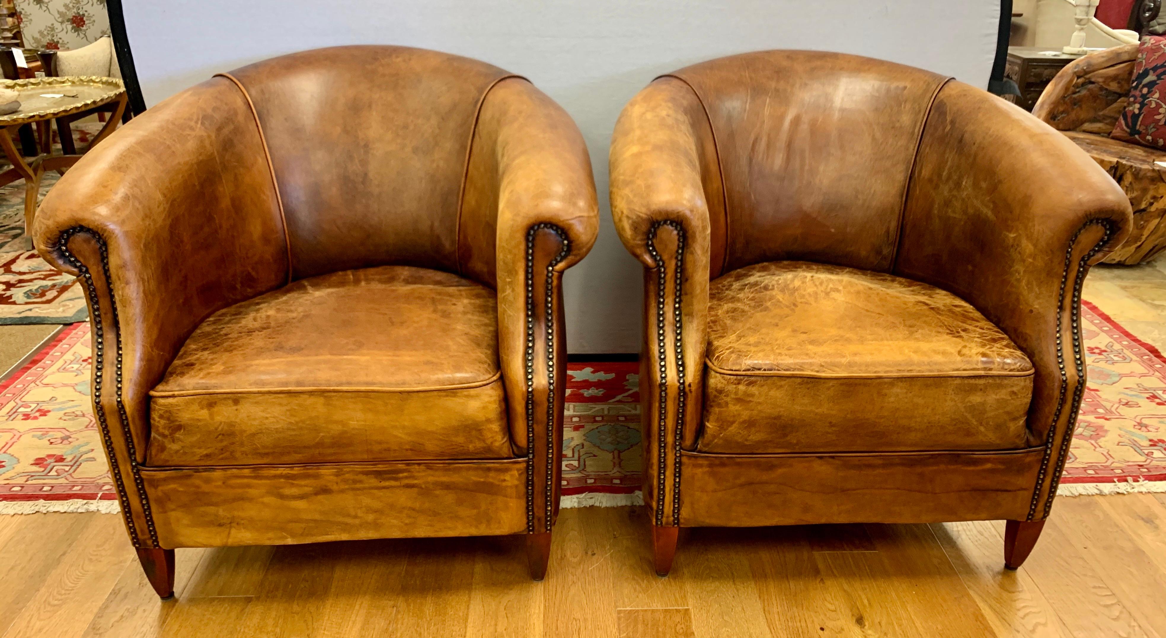 Elegant matching pair of distressed leather with nailheads chairs with coveted barrel back shape,
circa mid-20th century or earlier. The brown leather has a gorgeous patina and is distressed and
has some cracking mostly at the seat as is the plan.