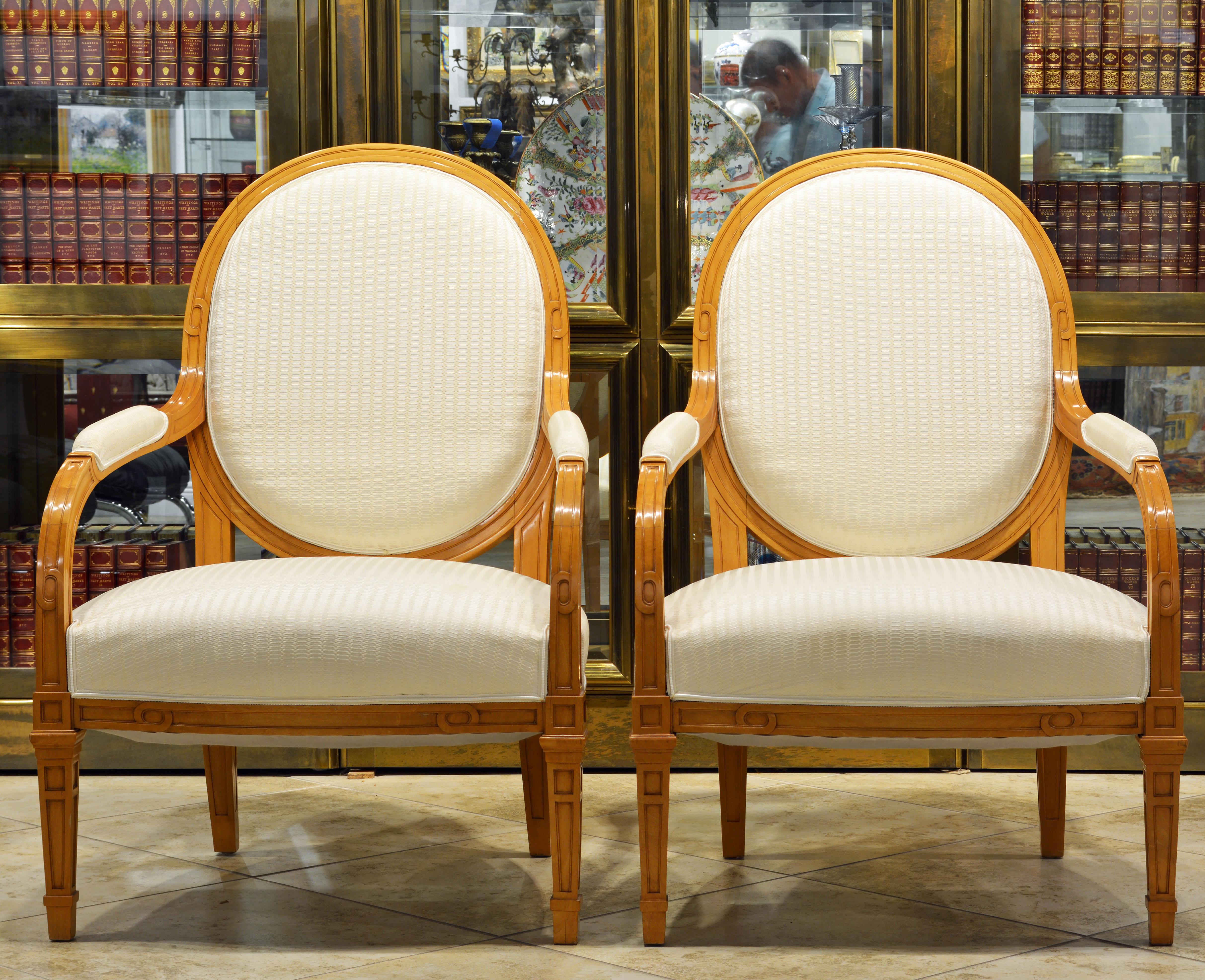 These satinwood oval back armchairs are fashioned in the Louis XVI style with detail and carved motifs reflecting the Art Deco era. Delicately covered by white structured fabric complimenting the blonde wood the gently restored chairs make an