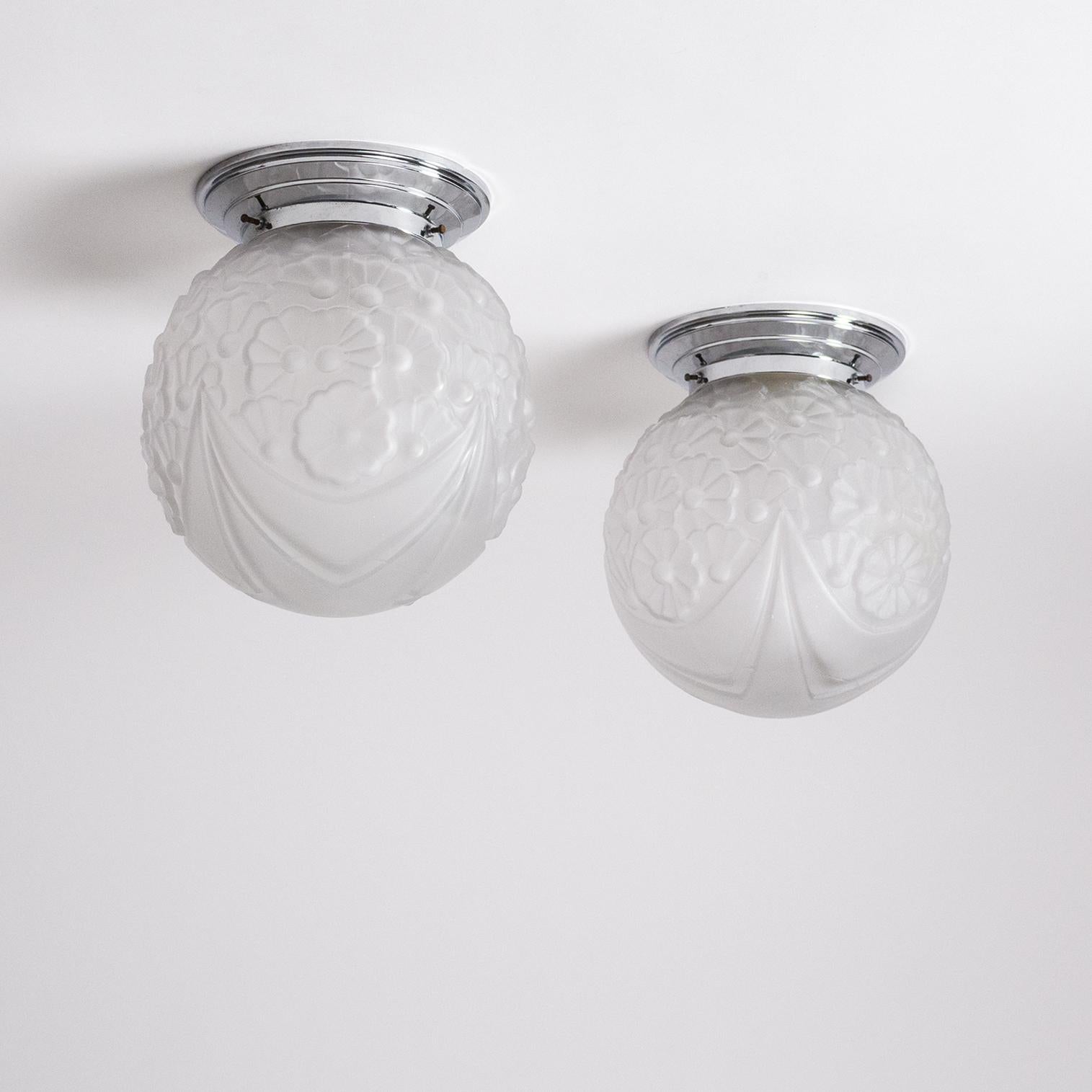 Fine pair of French Art Deco flush mounts from the 1930s. Attached to a chrome base is a thick pressed glass globe with an intricate floral and geometric design and a satin finish. Good original condition with minor wear to the chrome and a chip on