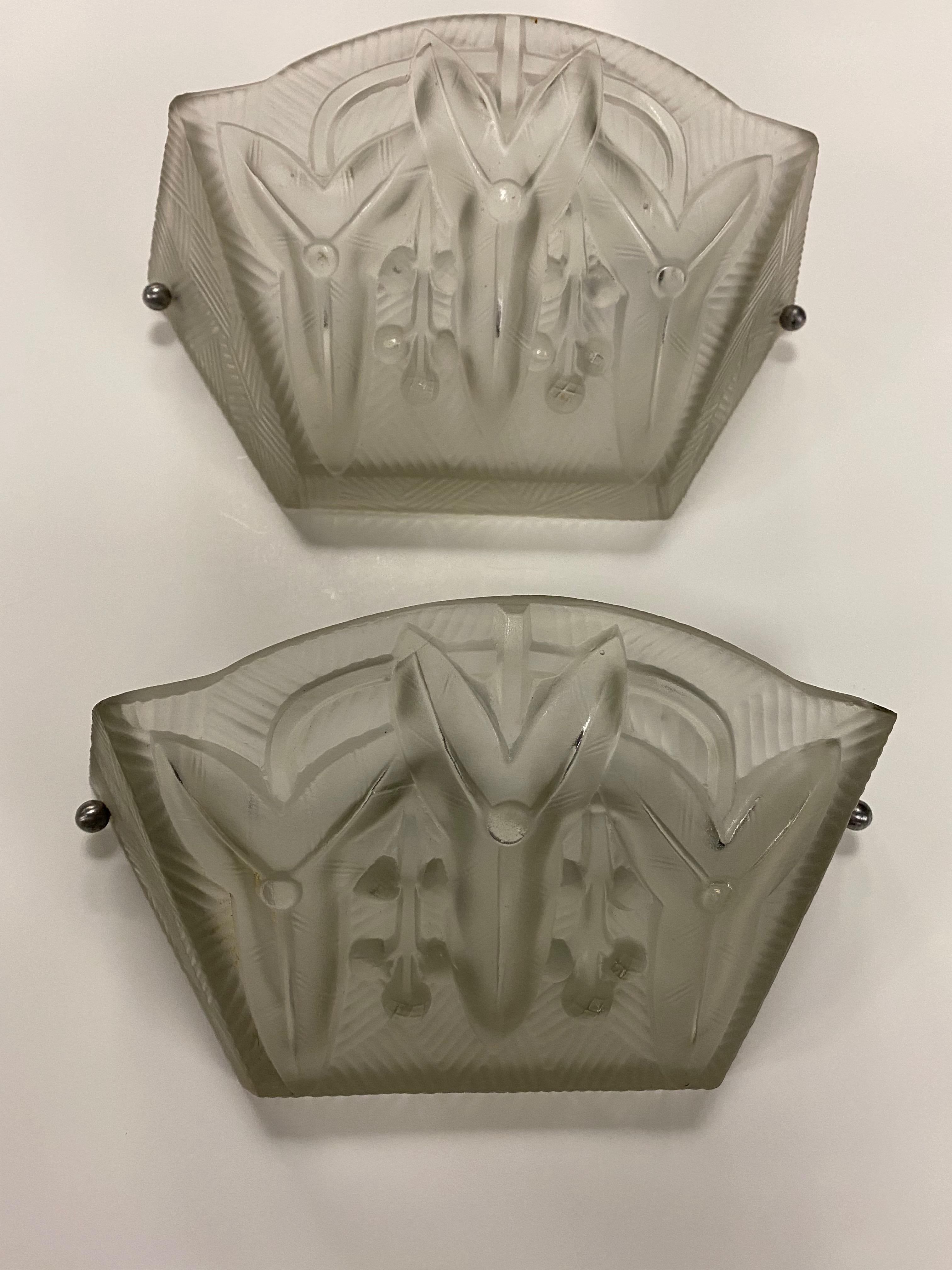 Pair of French Art Deco wall sconces signed by French designer Jean Noverdy. Having clear and frosted glass shades with geometric motif. Held by a frameless bracket. Has been rewired for American use with one candelabra socket. Each socket has a max