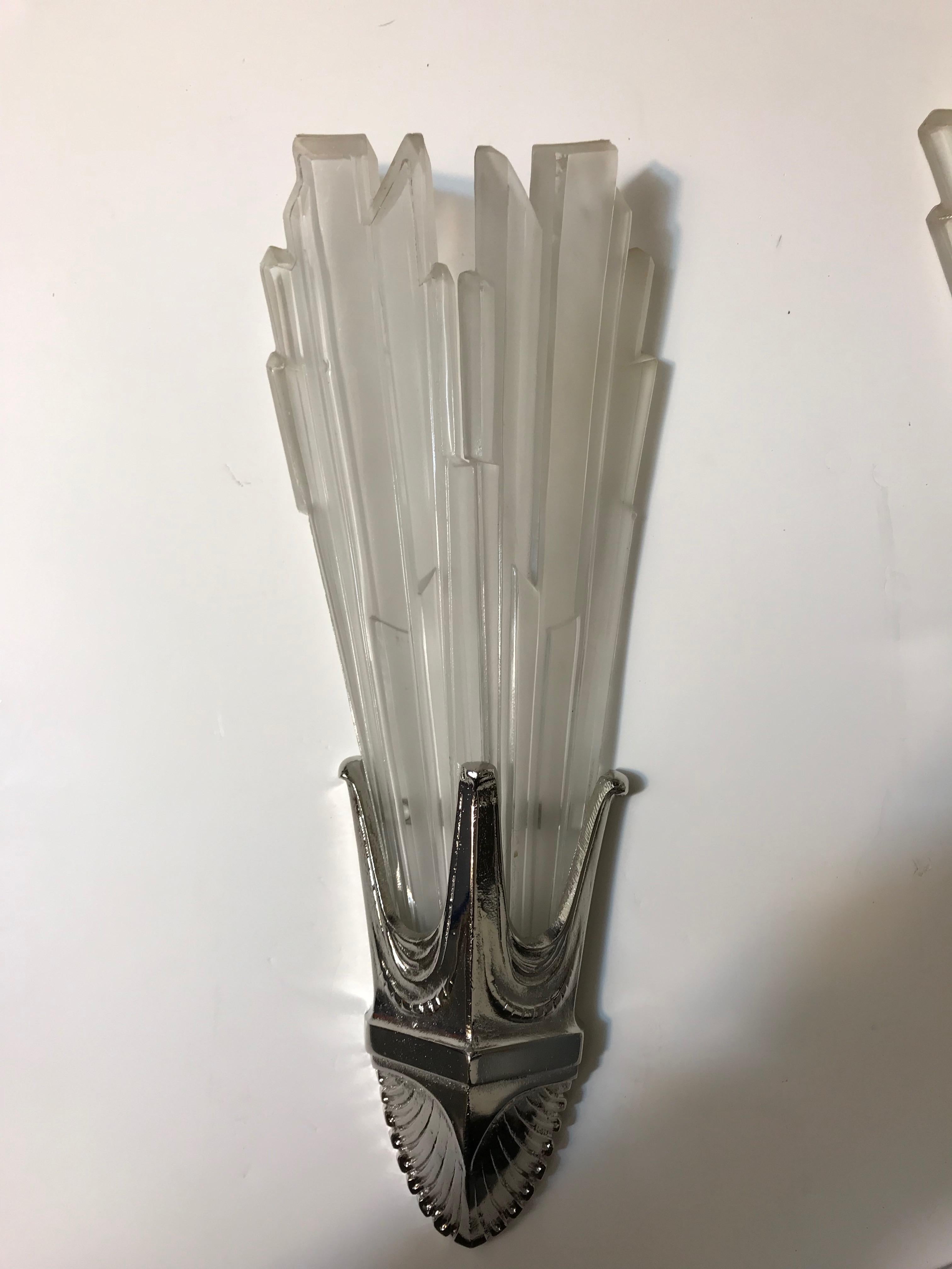 Pair of French Art Deco sconces by G Leleu. Having clear frosted glass shades with geometric motif details throughout. Held by polished nickel geometric design frames. Has been rewired for American use. Each sconce takes one 60 watt candelabra