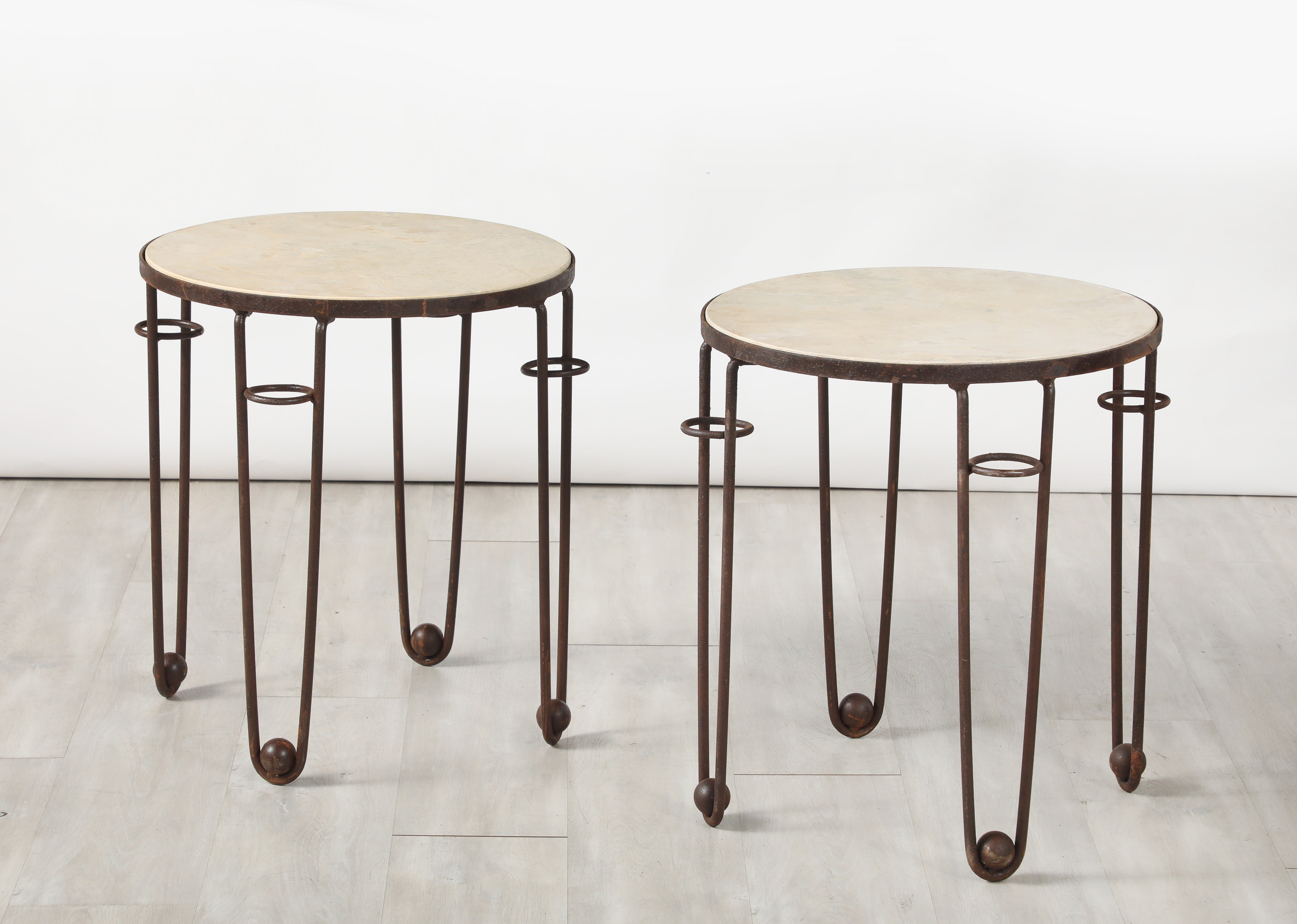 Paire de tables d'appoint circulaires en fer forgé Art Déco avec plateaux en travertin.  Quatre pieds en épingle à cheveux avec des éléments de motifs circulaires et des pieds en boule.  
France, vers 1940 
Taille : 22 1/4