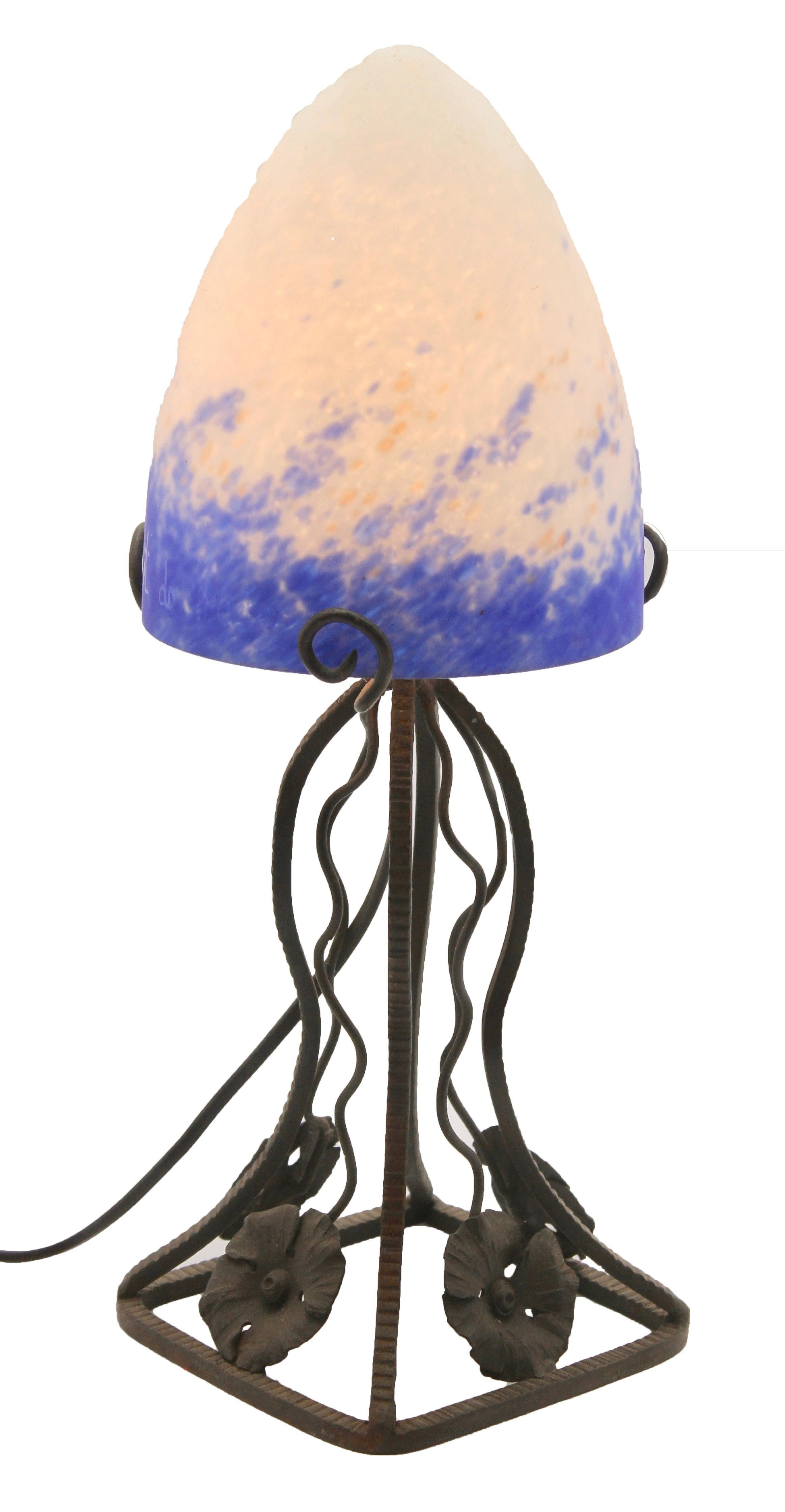 A wonderful pair of French lamps. The stands are handmade in wrought iron with black finish patina and hammered with floral pattern. The metalwork is of excellent quality.
They are crowned with bright colored shades in mottled glass paste with blue