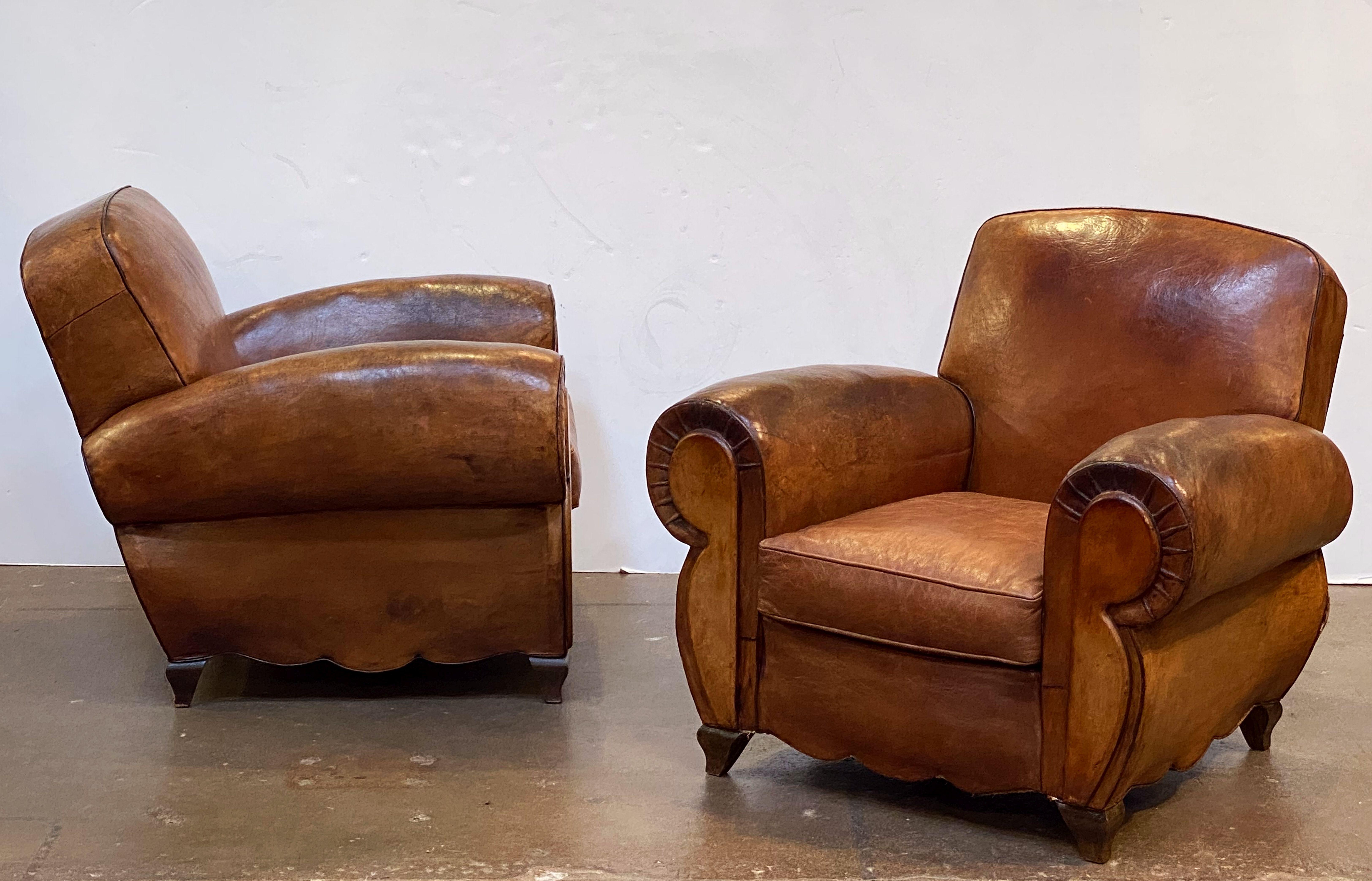 A handsome pair of vintage French leather upholstered club or lounge chairs, each chair featuring a comfortable back and seat with removable cushion, with stylish arms and original leather, brass nail-head trim to back and resting on shaped