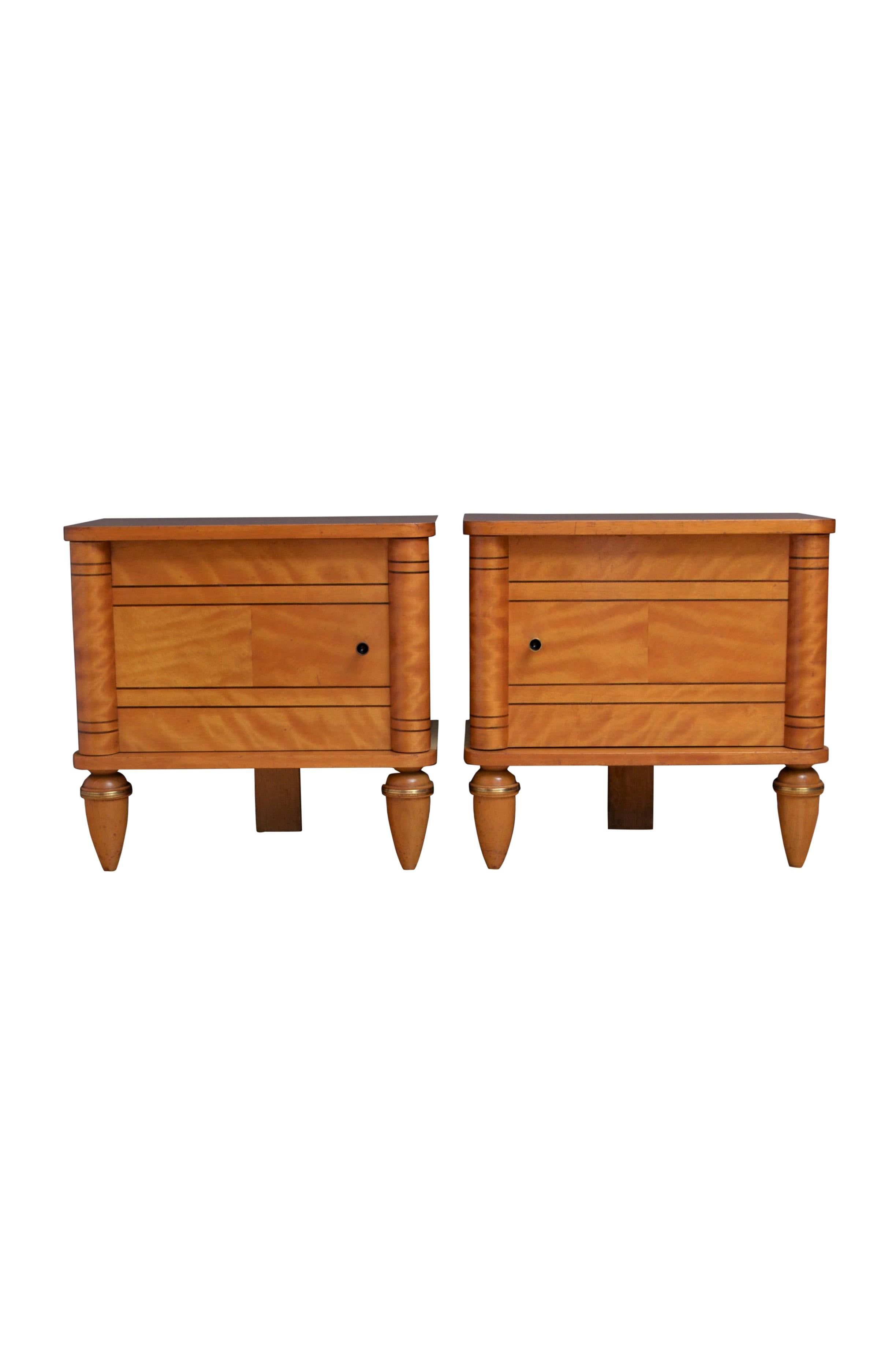 K0570 Attractive satin birch bedside cupboards, each having oversailing top with rounded corners above string inlaid door fitted with original handle and flanked by half columns, standing on turned, tapered legs with brass ring. This antique pair of