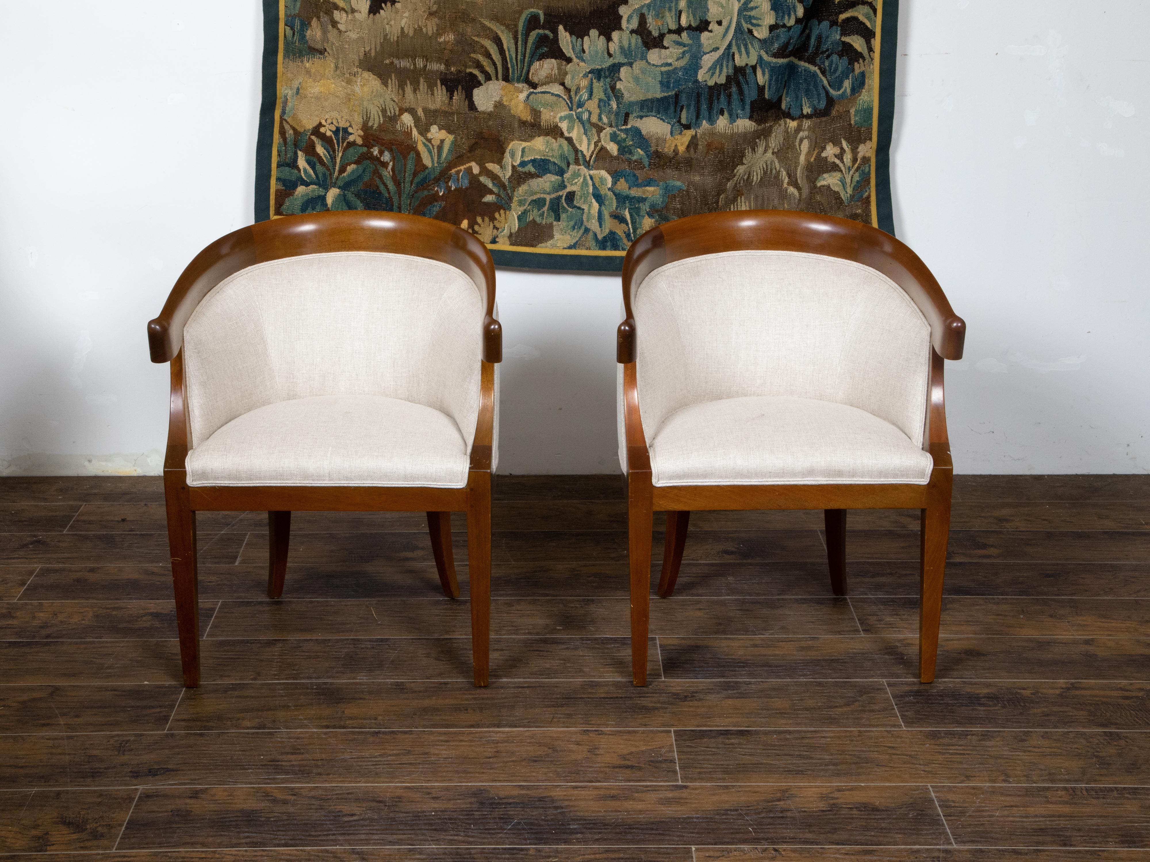 A pair of French Art Deco period walnut armchairs from the early 20th century, with horseshoe back, saber legs and linen upholstery. Created in France during the Art Deco period in the second quarter of the 20th century, each of this pair of walnut