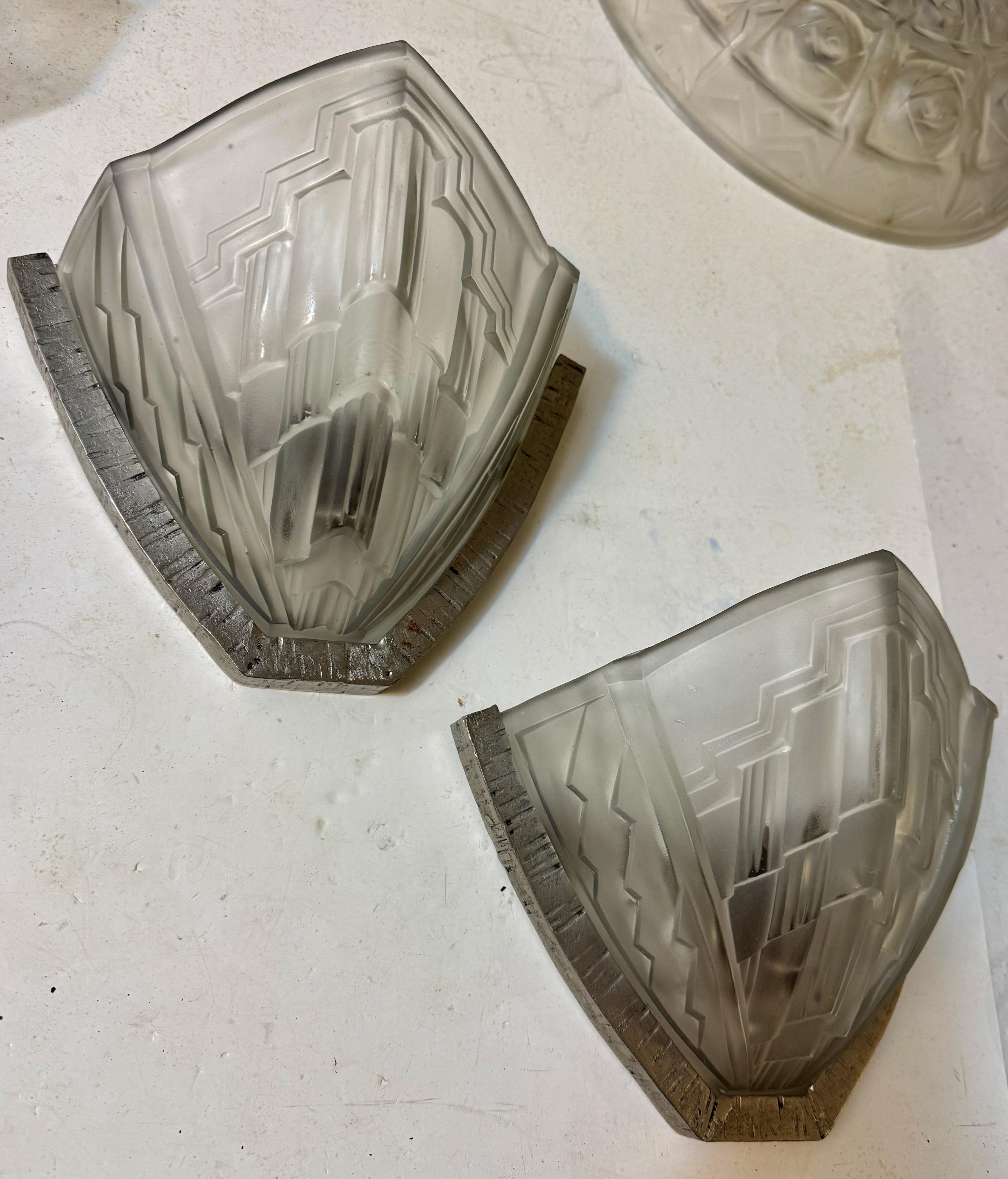 Pair of French of Art Deco sconces signed by Noverdy. Having clear frosted glass shades with a geometric motif. Held by Nickel wrought iron frames. Frames have been re plated in a polish nickel.  Has been rewired for American use with one