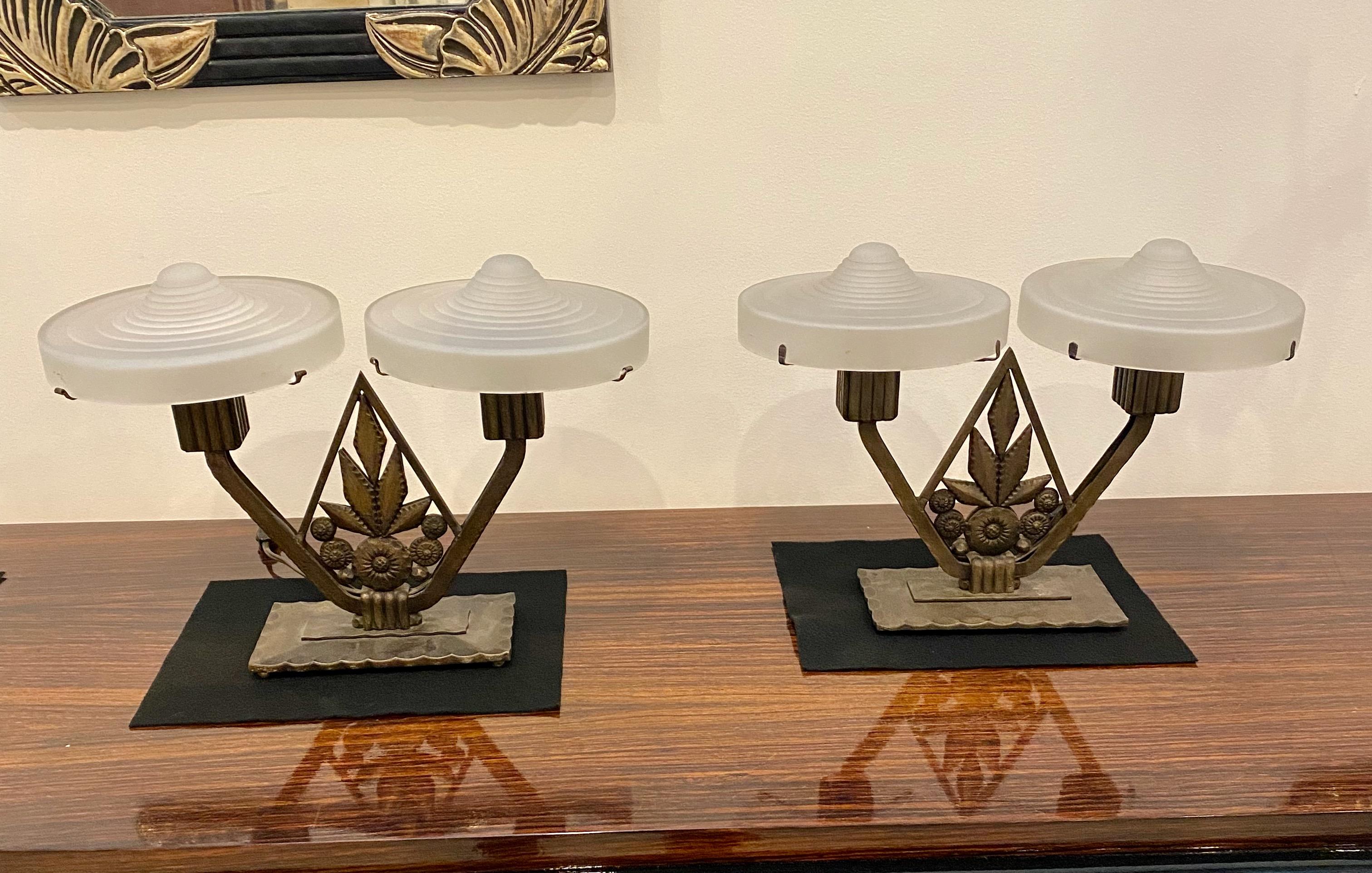 Ein Paar französische Art Deco Tischlampen mit geometrischem Motiv. Vier klare, mattierte, gestufte Glasschirme ruhen auf einem geometrischen Deko-Rahmen mit Bronzepatina. Der Sockel ist durchgehend mit geometrischen Motiven versehen. Wurde für den