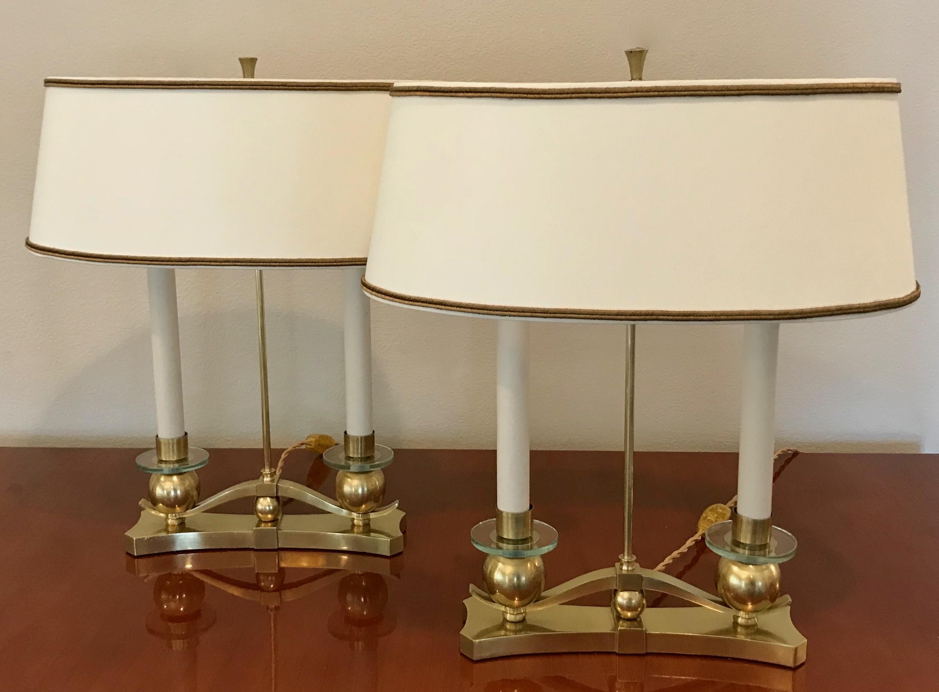 A beautiful pair of French Art Deco or Moderne style table or bouillotte lamps. Distinctive S-curved rests atop a brass ball and repeats this motif supporting two candle arms with glass bobeche. Oval shaped shades allow for more narrow use such as