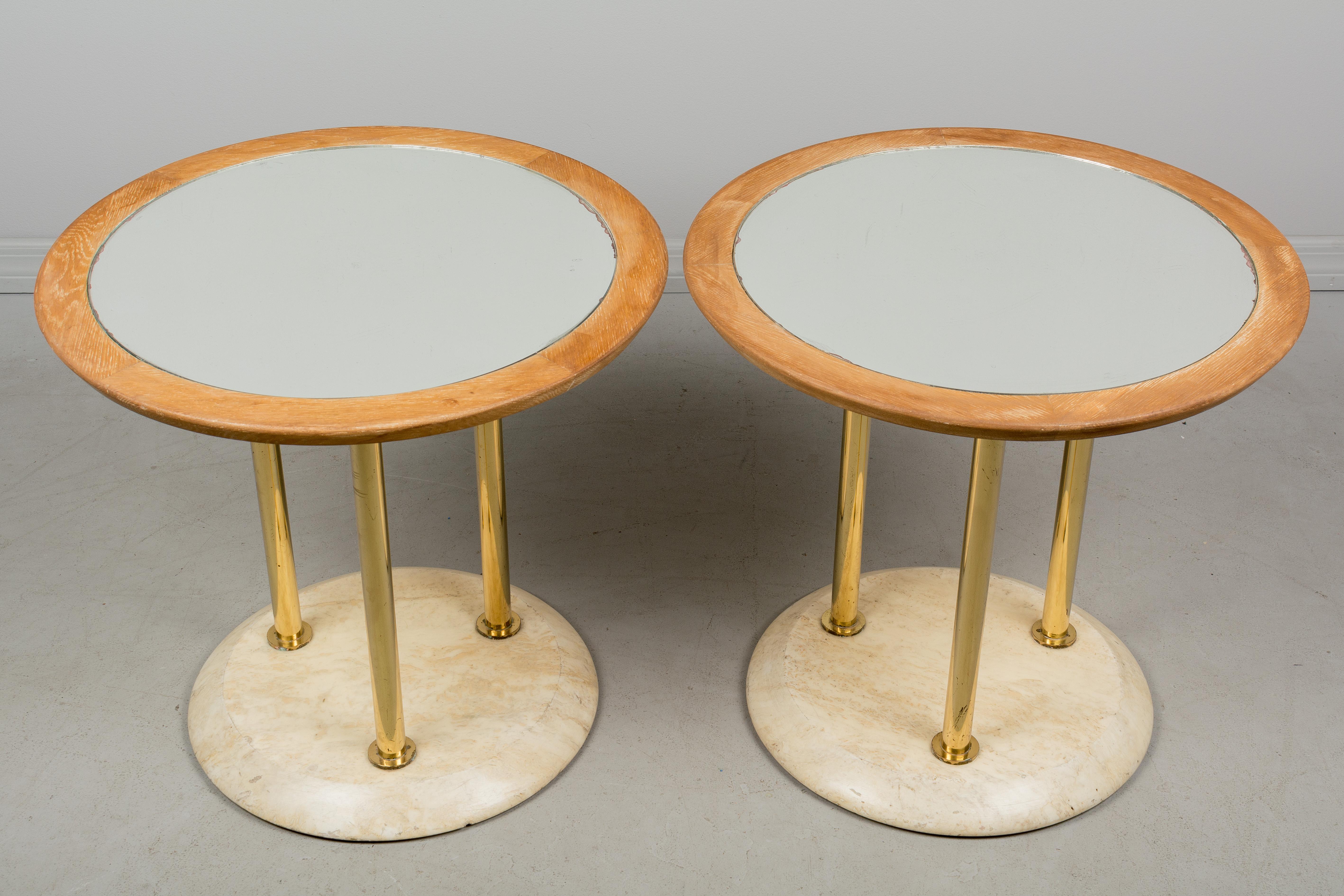 A pair of French Art Deco guéridon cocktail tables with circular wood tops inset with mirror, tubular brass legs and travertine base. Mirrors are scratched especially around the perimeter. Weight: 51 lbs. each.
