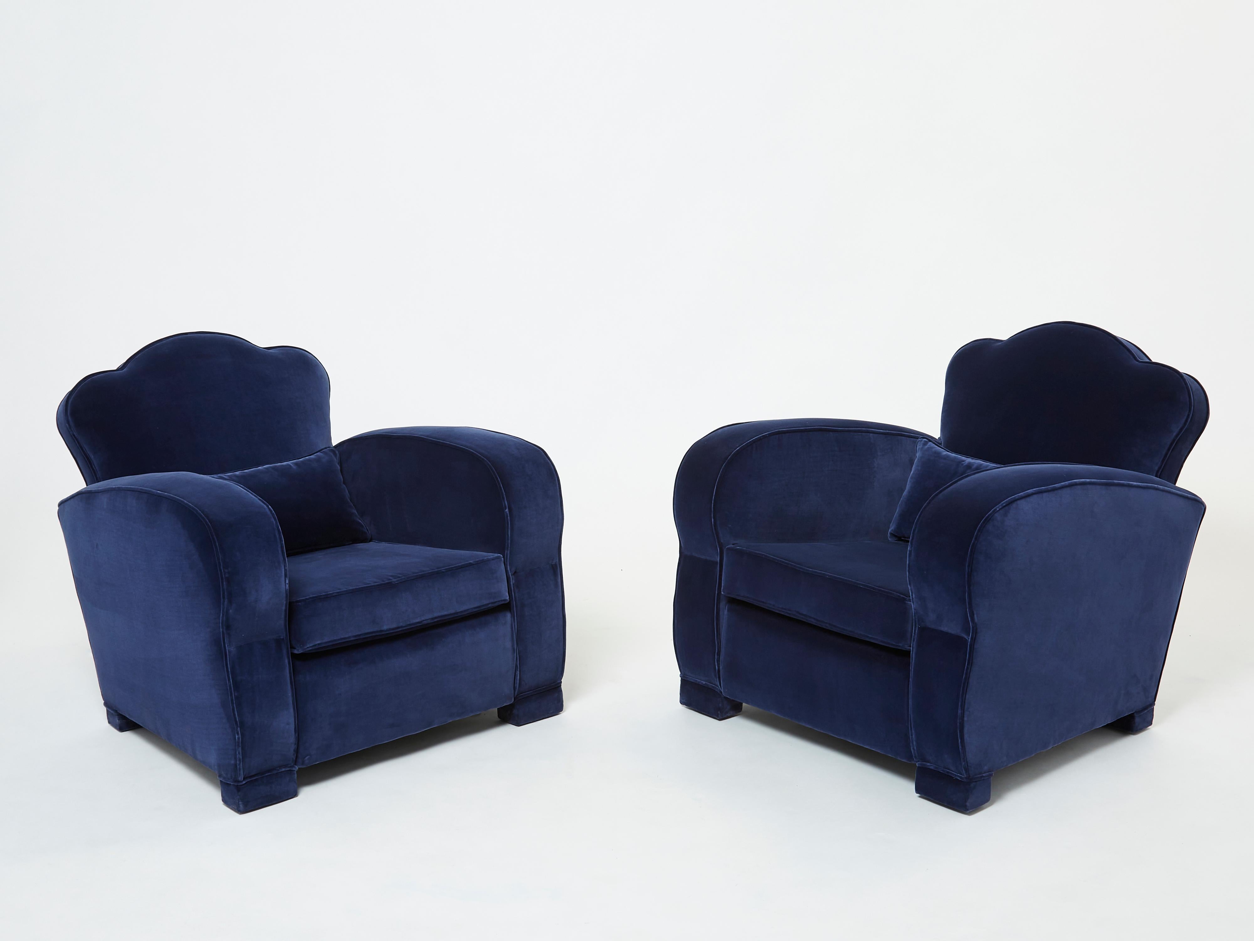 This pair of armchairs embodies the smooth lines of the Art Deco club chairs that came from the French 1940s, and are attributed to Jules Leleu. New upholstery in a deep blue velvet enhances the pair’s original, beautiful shape, while plush cushions