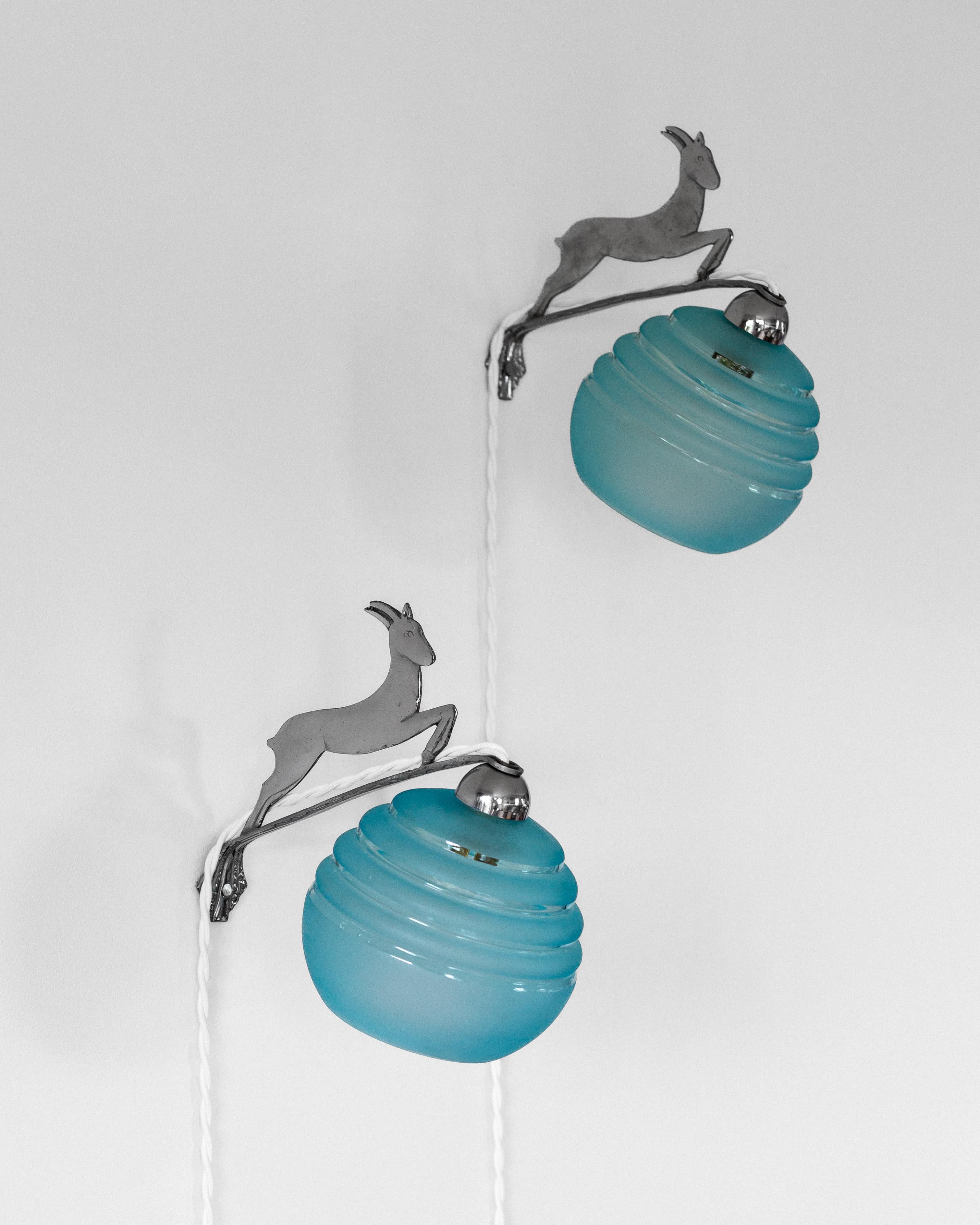 A pair of original Art Deco wall lights from France, featuring chrome bases with jumping deer designs, each holding a ribbed blue glass globe. Crafted in the 1930s and in great condition.

• Rewired with white twisted textile cords, switches, and EU