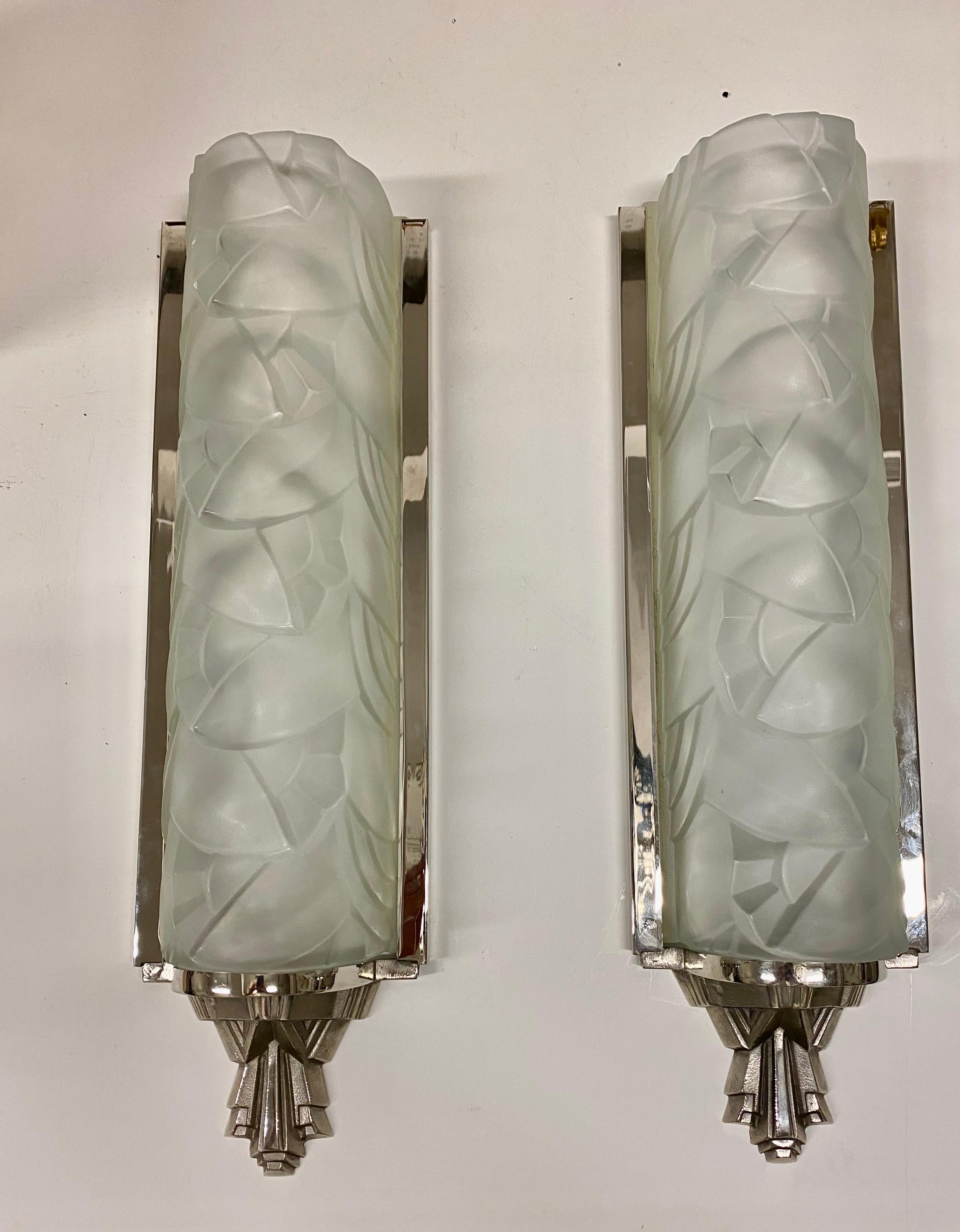 Grand pair of French Art Deco wall sconces by the French artist “Degue”. Having clear frosted glass shades with geometric and floral motif. Held in a geometric deco design frame in nickel. Each shade is marked Degue. Has been rewired for American