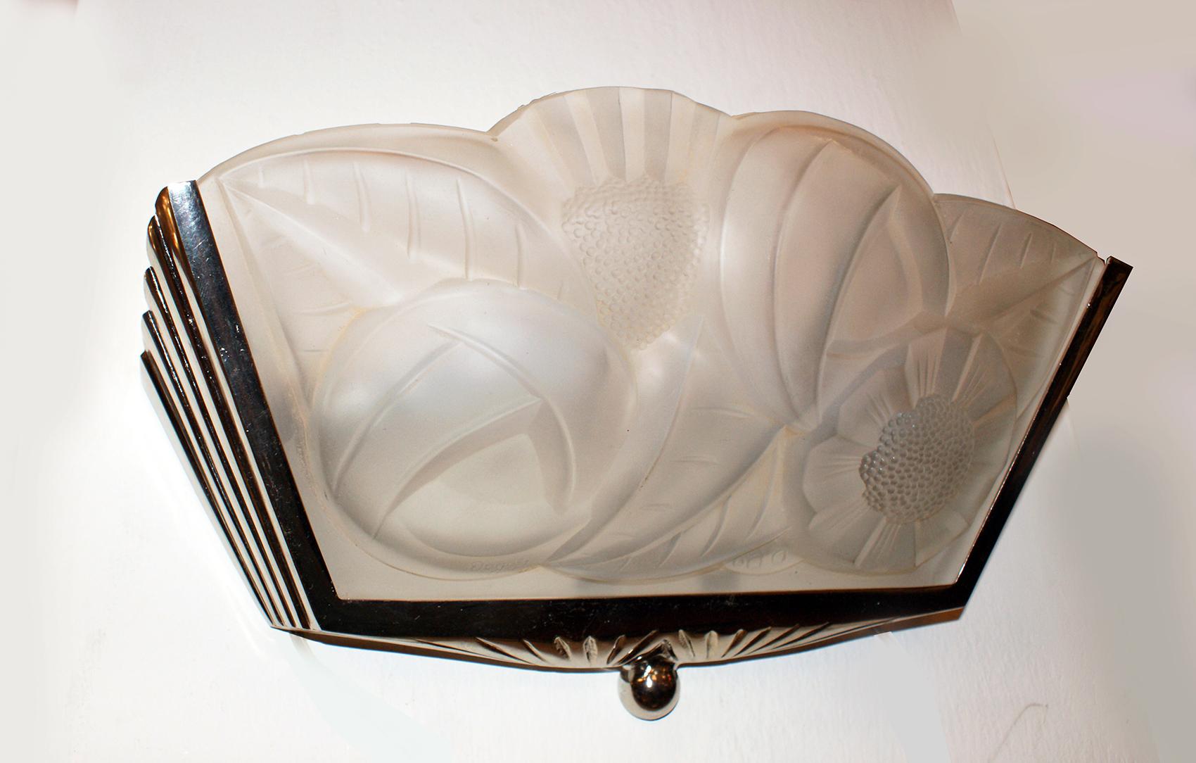 Stunning pair of French Art Deco wall scones signed by the French artist Degué (David Gueron). 
The panels are in molded clear frosted glass with floral motif design, held by a geometric nickel polished frame. 
Having two candelabra sockets in