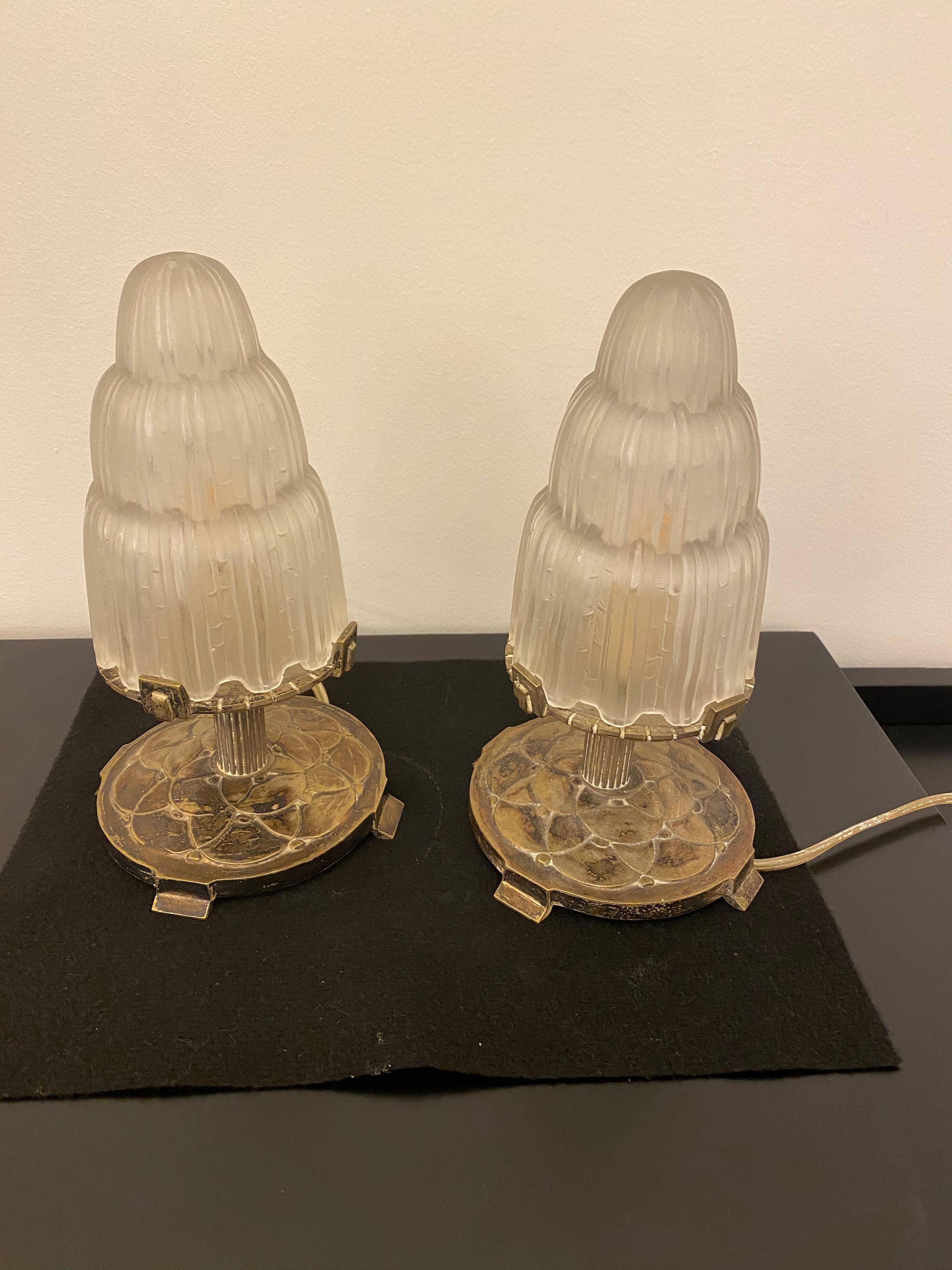 Pair of French Art Deco table lamps created by Marius Ernest Sabino, (1878-1961). The shades are clear frosted glass with polished details referred to as the 