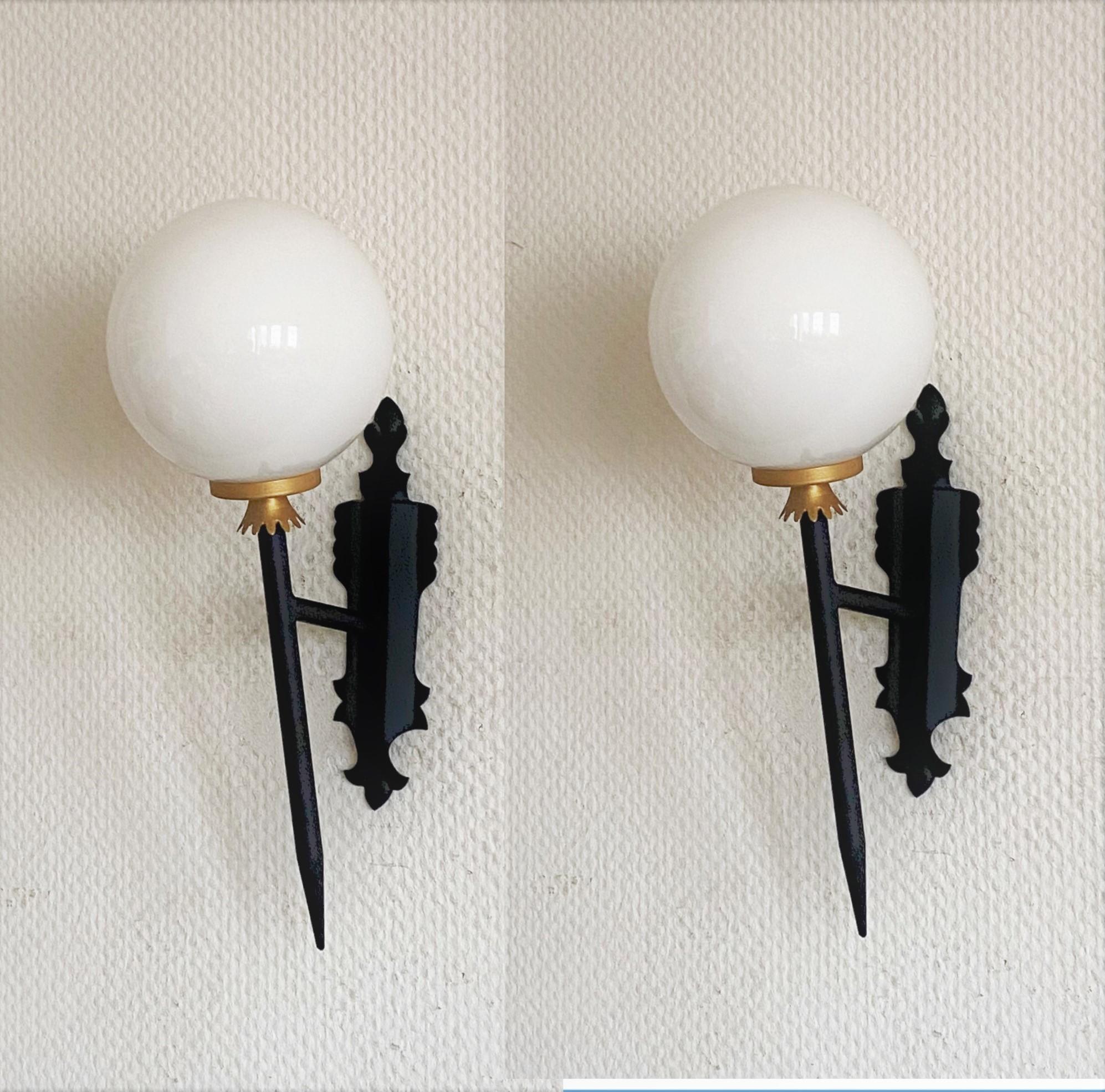A very elegant pair of Arte Deco black painted wrought iron parcel brass torchiere wall lights with opaline glass ball globes, for indoor and outdoor use, France, 1950s. 
The wall sconces are in very good condition, beautiful patina, rewired (glass