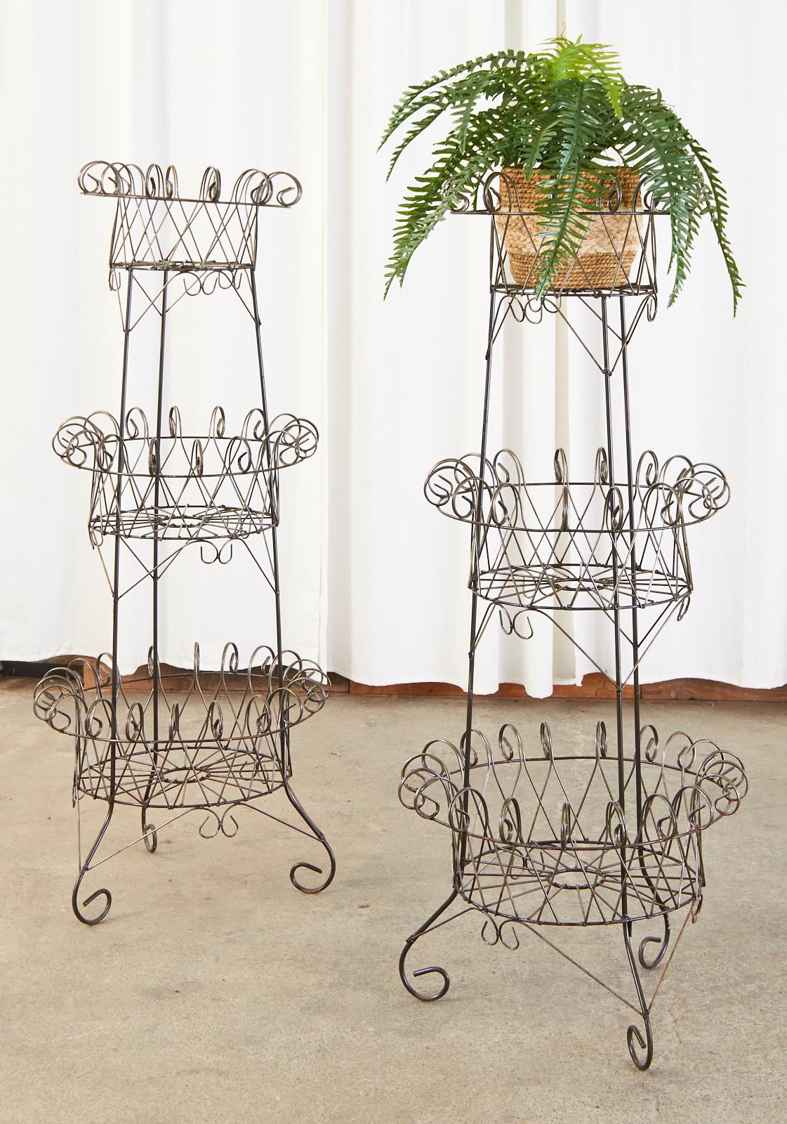 Grand pair of matching French iron and wire garden plant stands or jardinaires made in the art nouveau style. Crafted from an iron frame with a three-tier basket form and embellished with whimsical wire ending with scrolls. Beautiful display pieces