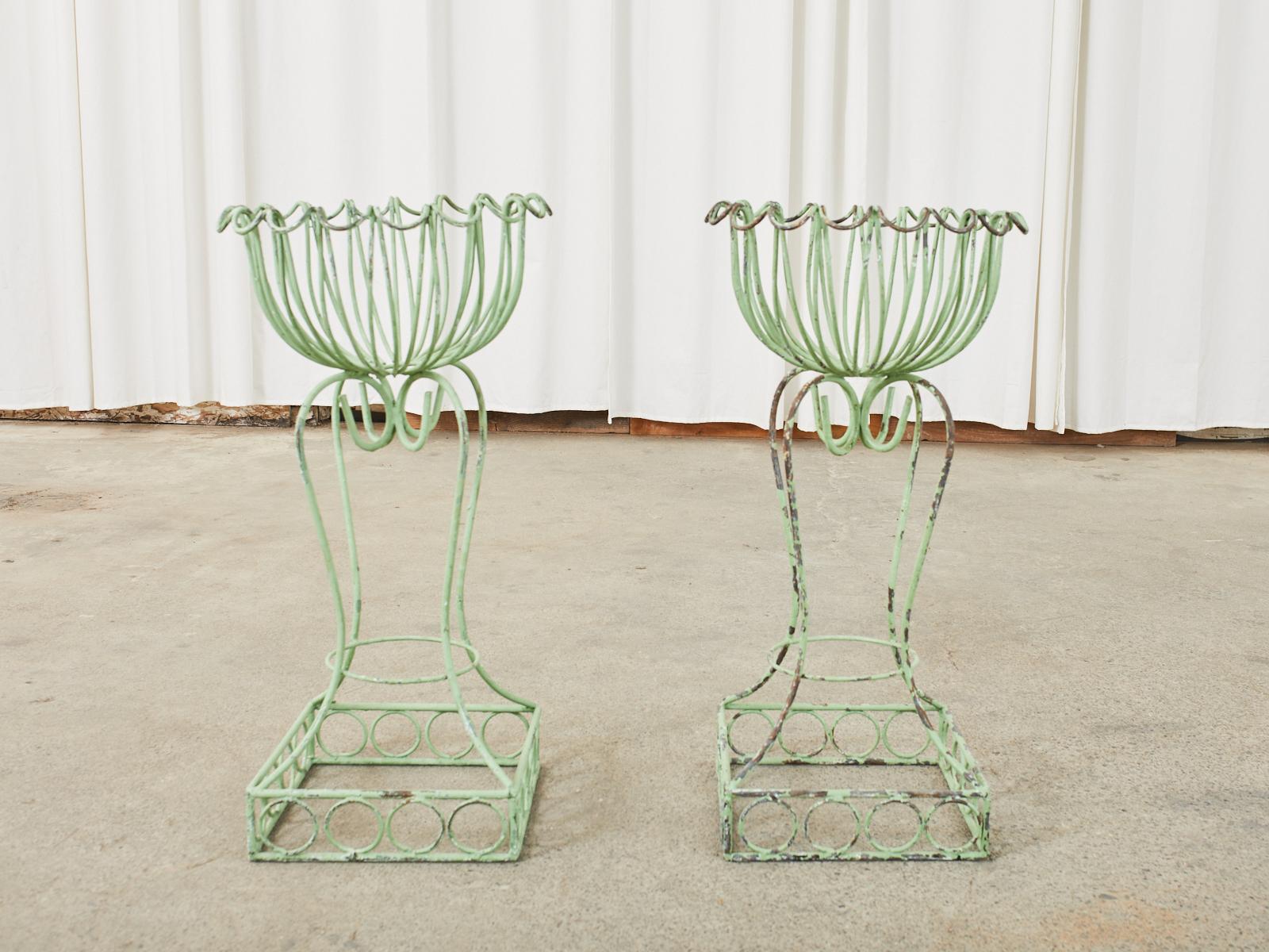Whimsical pair of French green garden planters or jardinieres crafted from iron wire. Made in the art nouveau style with a top basket having scalloped edges. Supported by a scrolled leg base with a square bottom. The iron is painted a seafoam green