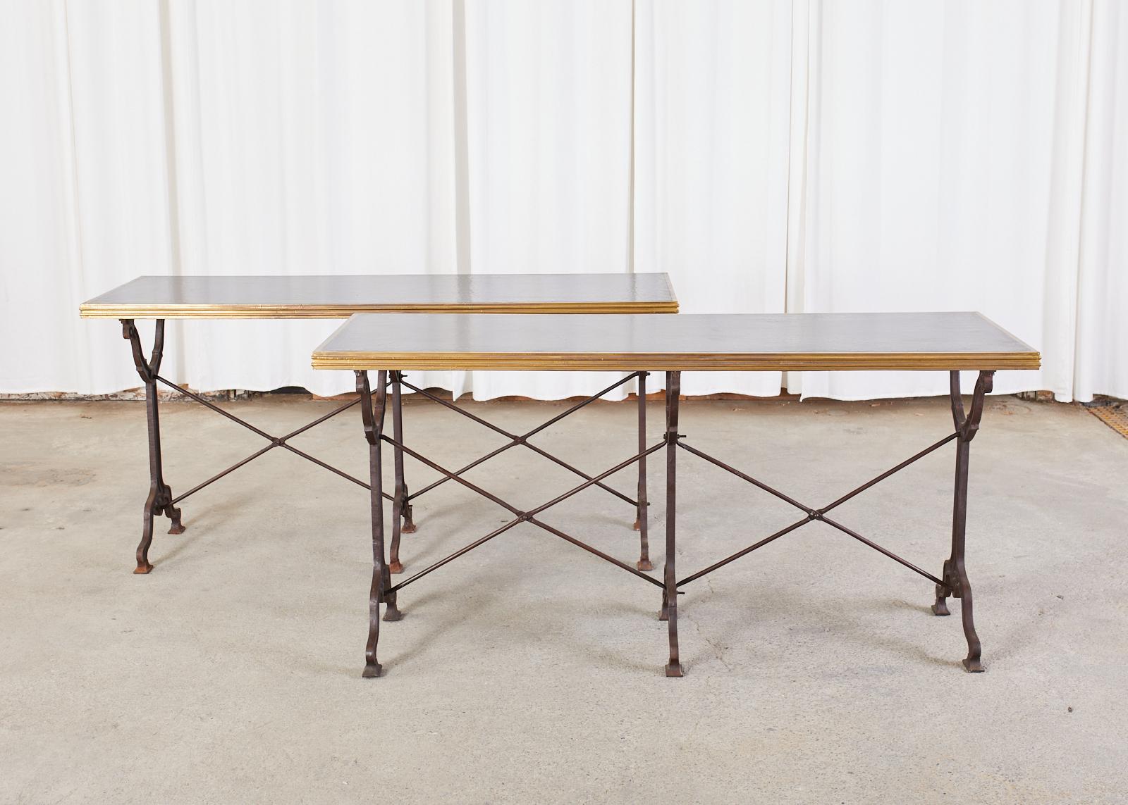 Matched pair of spectacular cafe or bistro dining tables featuring French art nouveau period style iron bases having triple pedestals and foundry signature on the sides. These tables have a metal clad top with a brass wrap around the border trim.