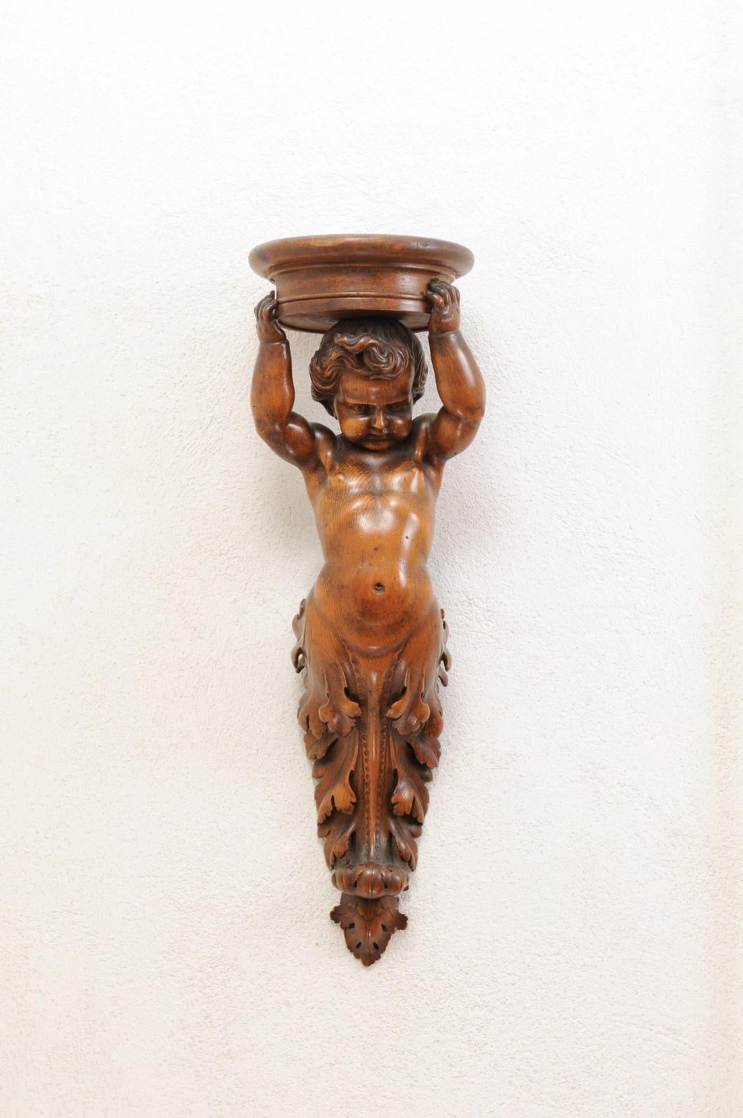 A pair of French Baroque style walnut wall sconces from the early 19th century, with carved putti. Created in France during the first decade of the 19th century, each of this pair of walnut sconces captures our attention with its carved putto