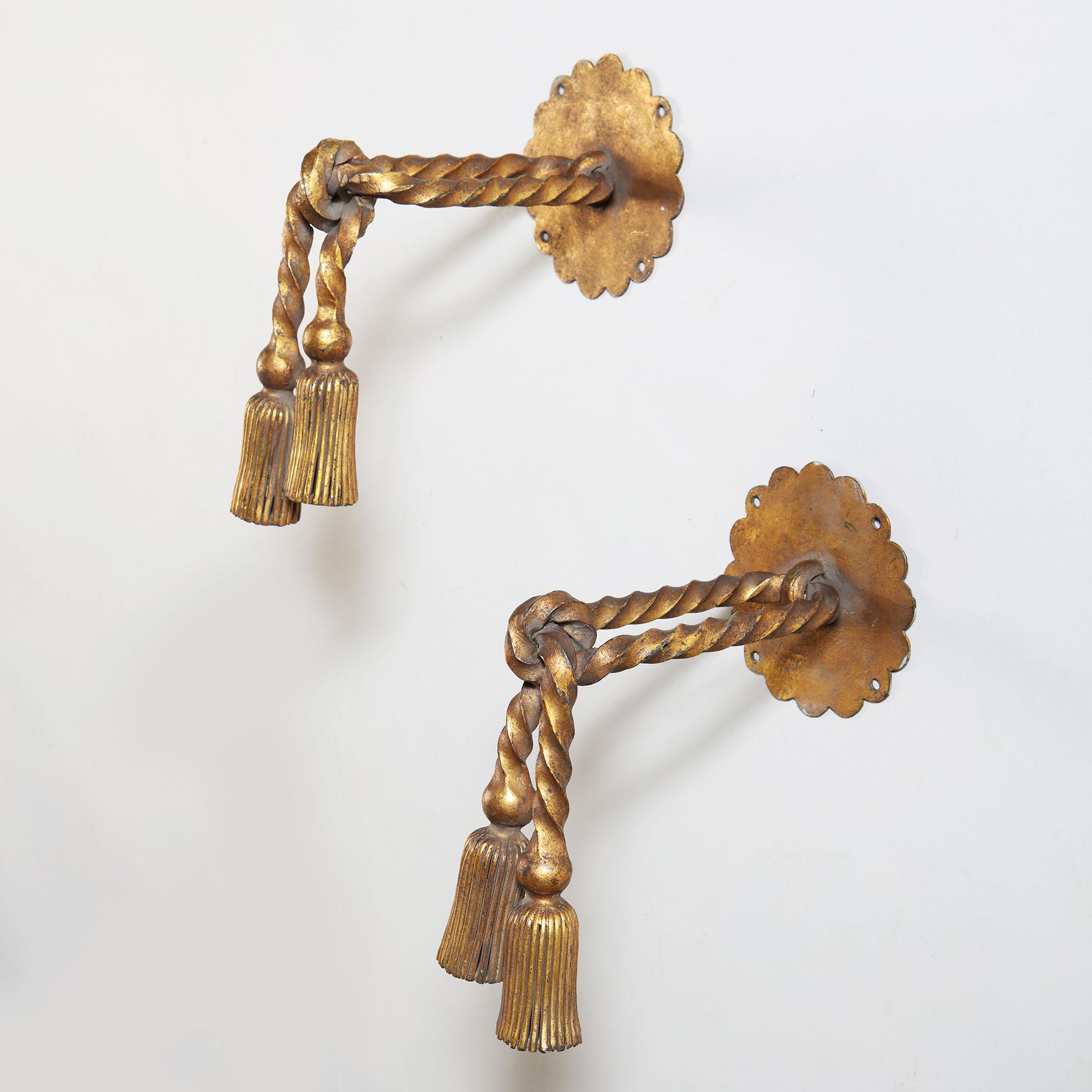 A fine pair of beaten bronze curtain tiebacks in the form of knotted twisted ropes with hanging tassels, attaching to the wall with a scalloped edge back plate. Attributed to Gilbert Poillerat (1902-1988).