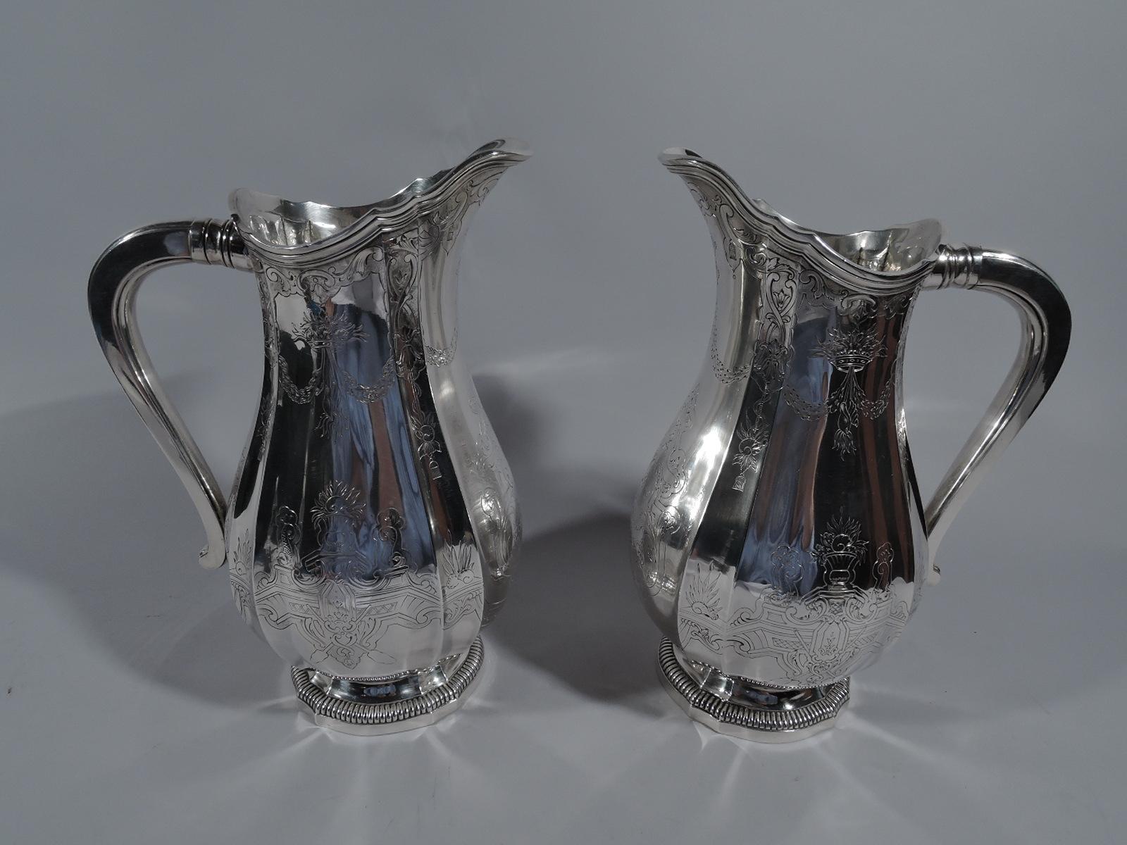 Pair of Belle Epoque Classical 950 silver water pitchers. Made by Paul Canaux in Paris, circa 1910. Each: Ovoid body with alternating curves and flutes, and scrolled helmet mouth. Foot stepped and same with gadrooning. Scroll handle. Engraved 18th