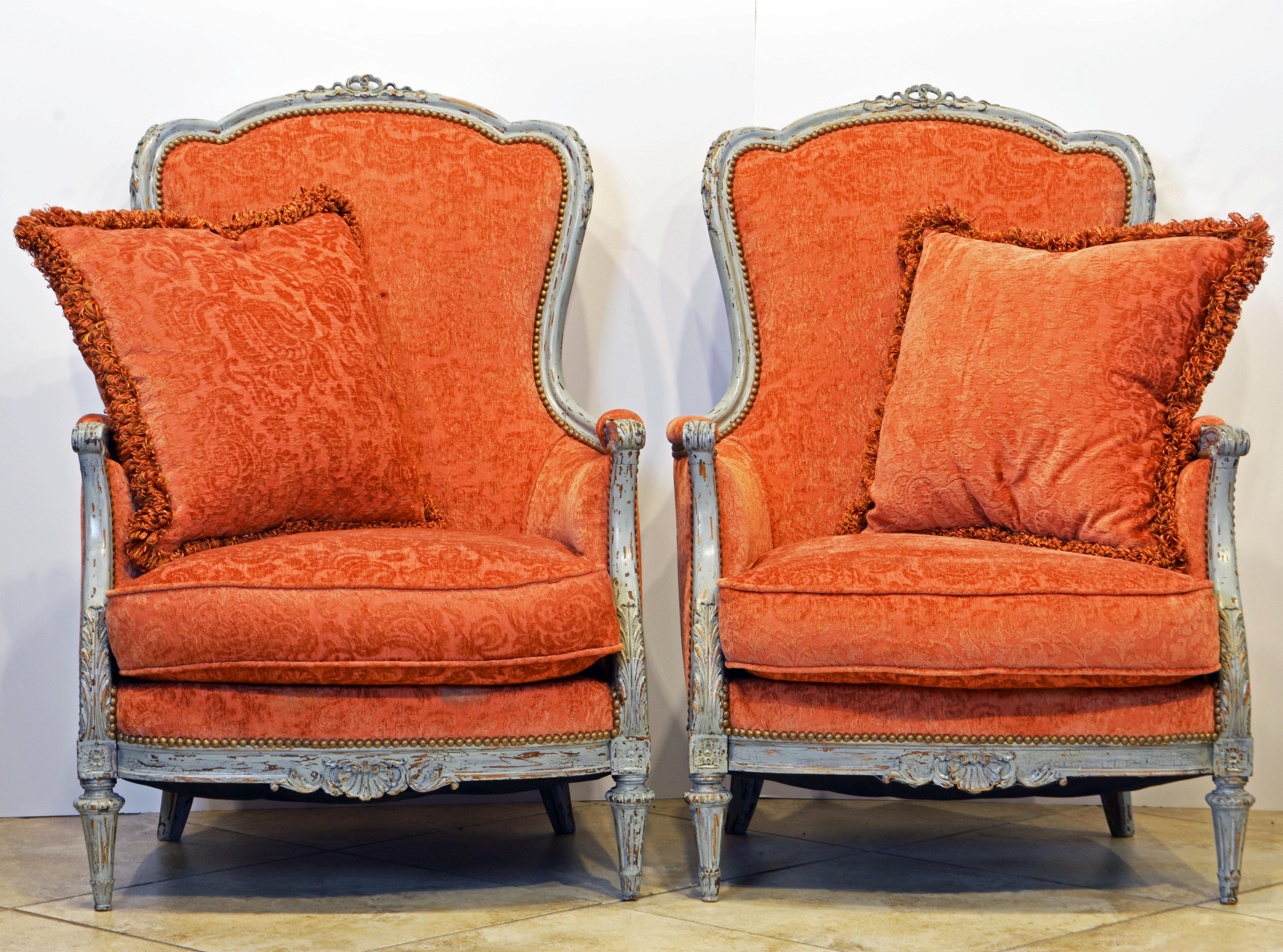 This elegant pair of French bergère chairs dating to the late 19th century (the Belle Époque period) feature upholstered backs and seats, closed sides with armrest pads and large pillows, circa 1880. The gray painted carved frames have romantic