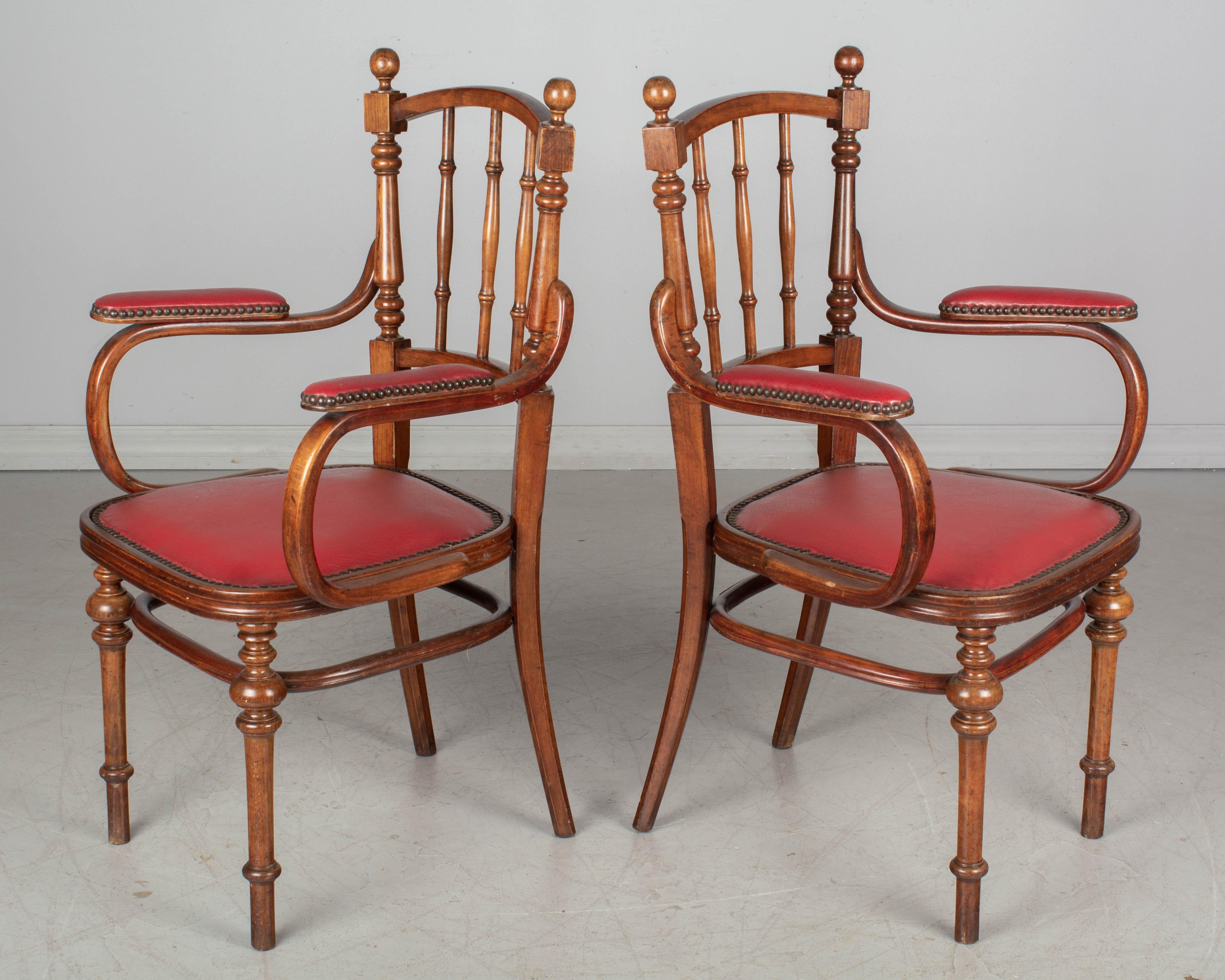 A pair of French Thonet style bentwood armchairs made of beechwood with turned legs and spindle back. Original red vinyl seat and armrests with nailhead trim.