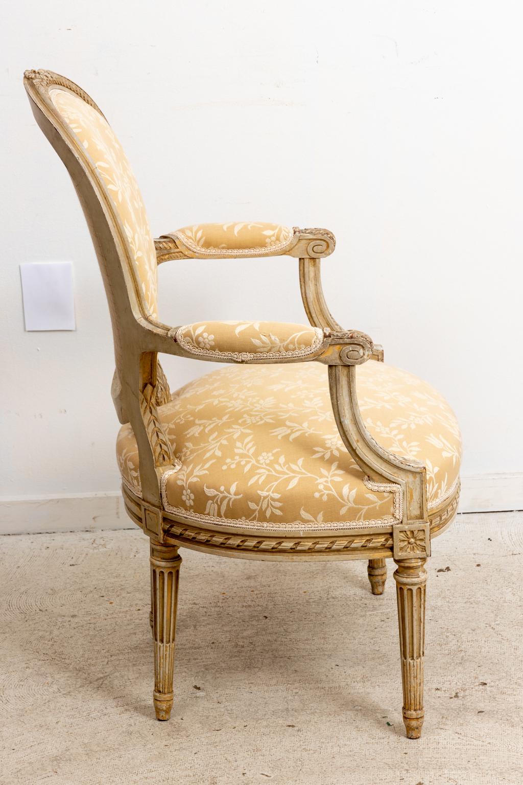 Pair of French Bergere chairs with oval seat back and upholstered armrests. The chair is further detailed with fluted, turned legs, scrolled arm holds, and carved ribbon banderol trim. Please note of wear consistent with age.