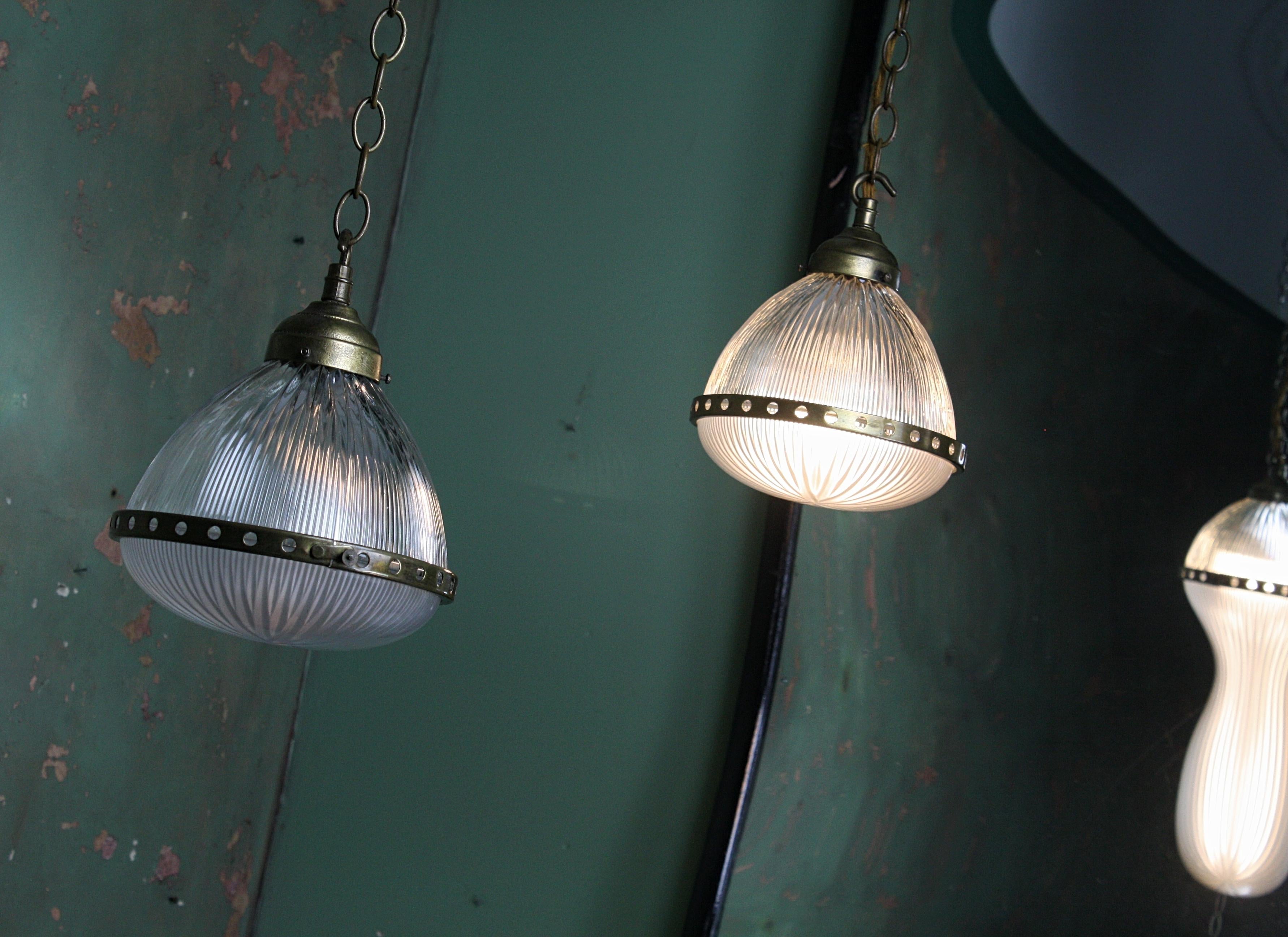 A fine pair of petite two part Holophane pendants, with heavy gauge cast galleries, brass central collar and age related brass chain, early 20th century.

Fine prismatic cut glass, with the Holophane stamp and model number, each light comes with