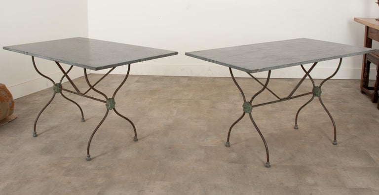 A pair of French bistro dining tables with Belgian Blue stone stone tops and iron bases in wonderful condition. The cast iron bases beautifully showcase folate designs and a great patina from years of outdoor use. Make sure to check out the detailed