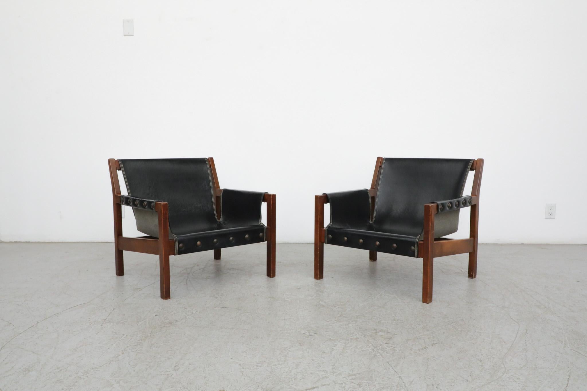Mid-Century pair of black leather and teak safari lounge chairs with brass stud accents. Handsome lounge chairs with striking style and surprising comfort! Not much is known about who the manufacturer may have been but they are wonderful and