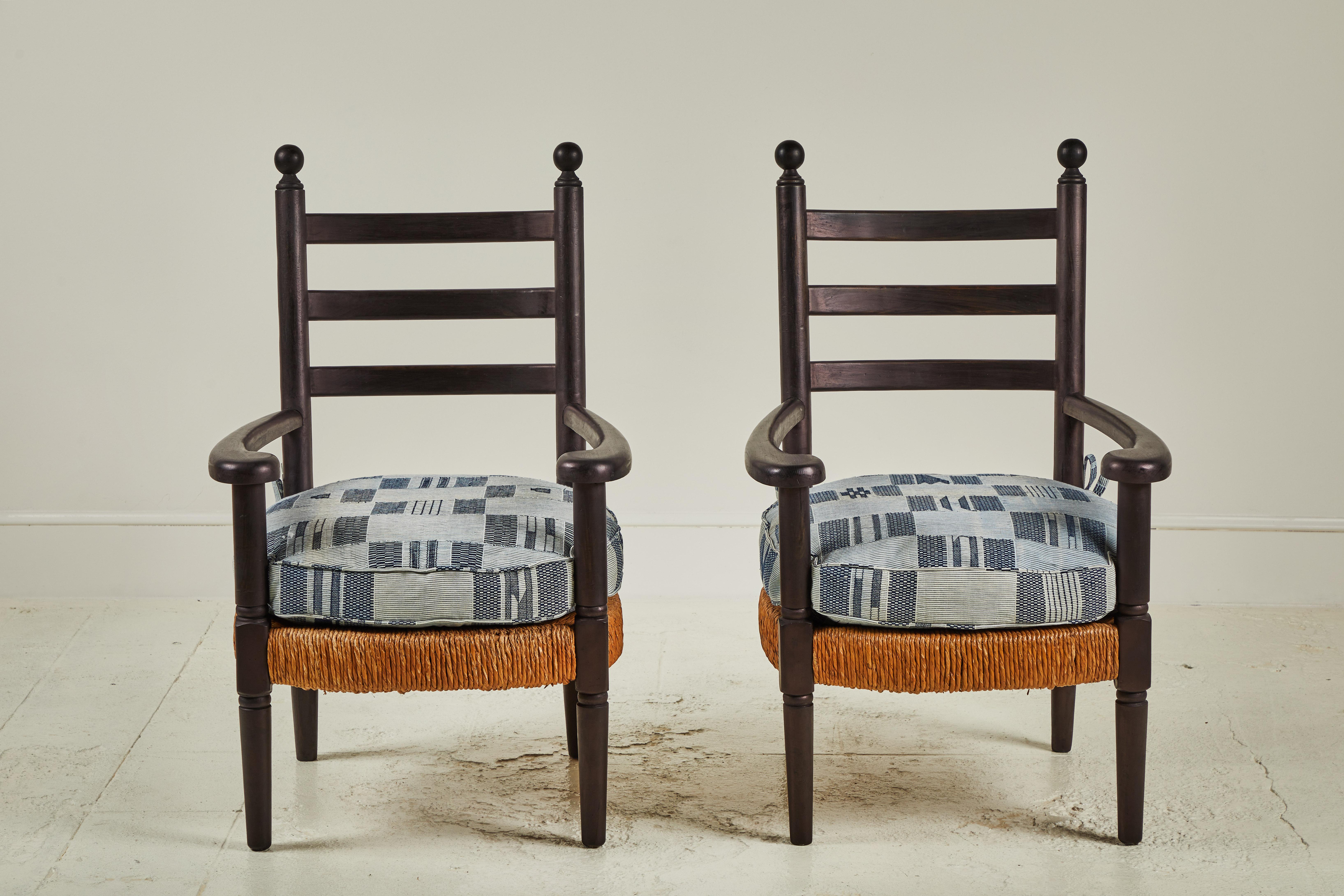 Pair of black wooden arm chairs with rush seats, blue and white seat cushions are made from vintage African textiles.