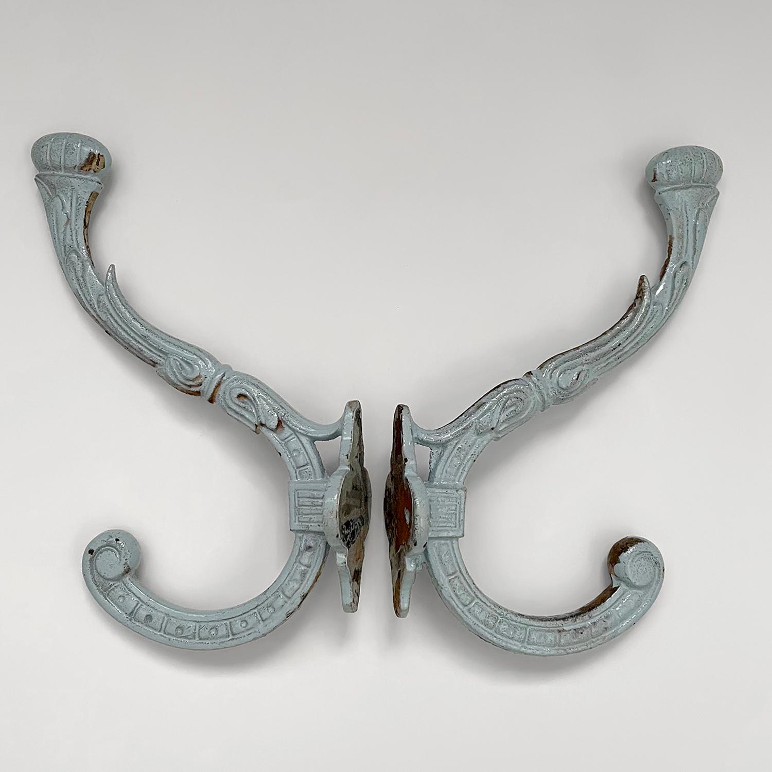 Pair of French enameled iron hooks
France, Early 20th century 
Pale French blue enamel paint has minor loss over stamped iron frame 
Wonderfully worn in and ready for years more love and service
Curved iron J hook finished with two hooks providing