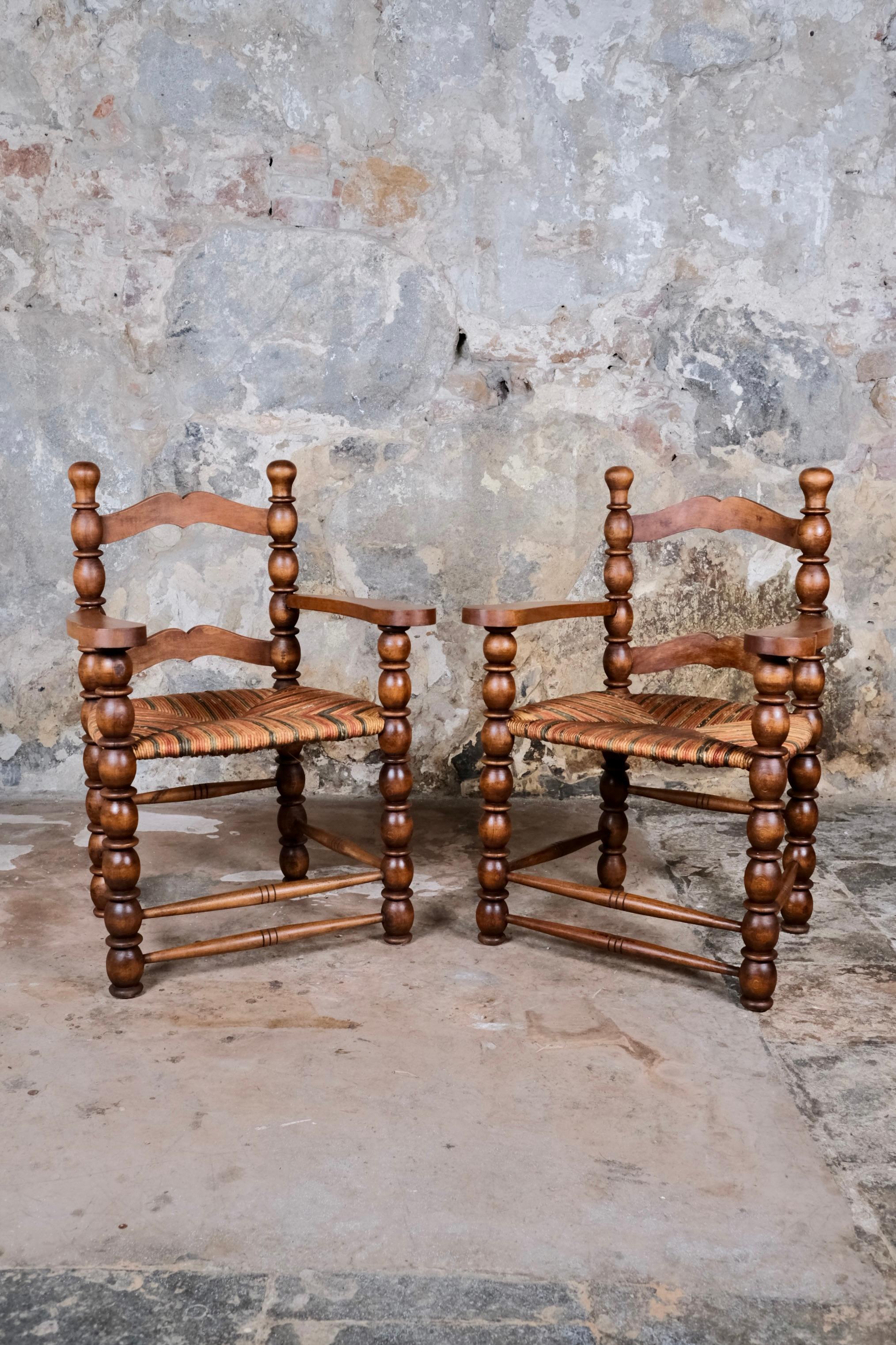 An exceptional and rare pair of French bobbin turned armchairs dating from the 1940s–1950s, crafted in solid oak with vibrant multicolored straw seats. Inspired by the distinctive design language of Charles Dudouyt, these chairs are a celebration of
