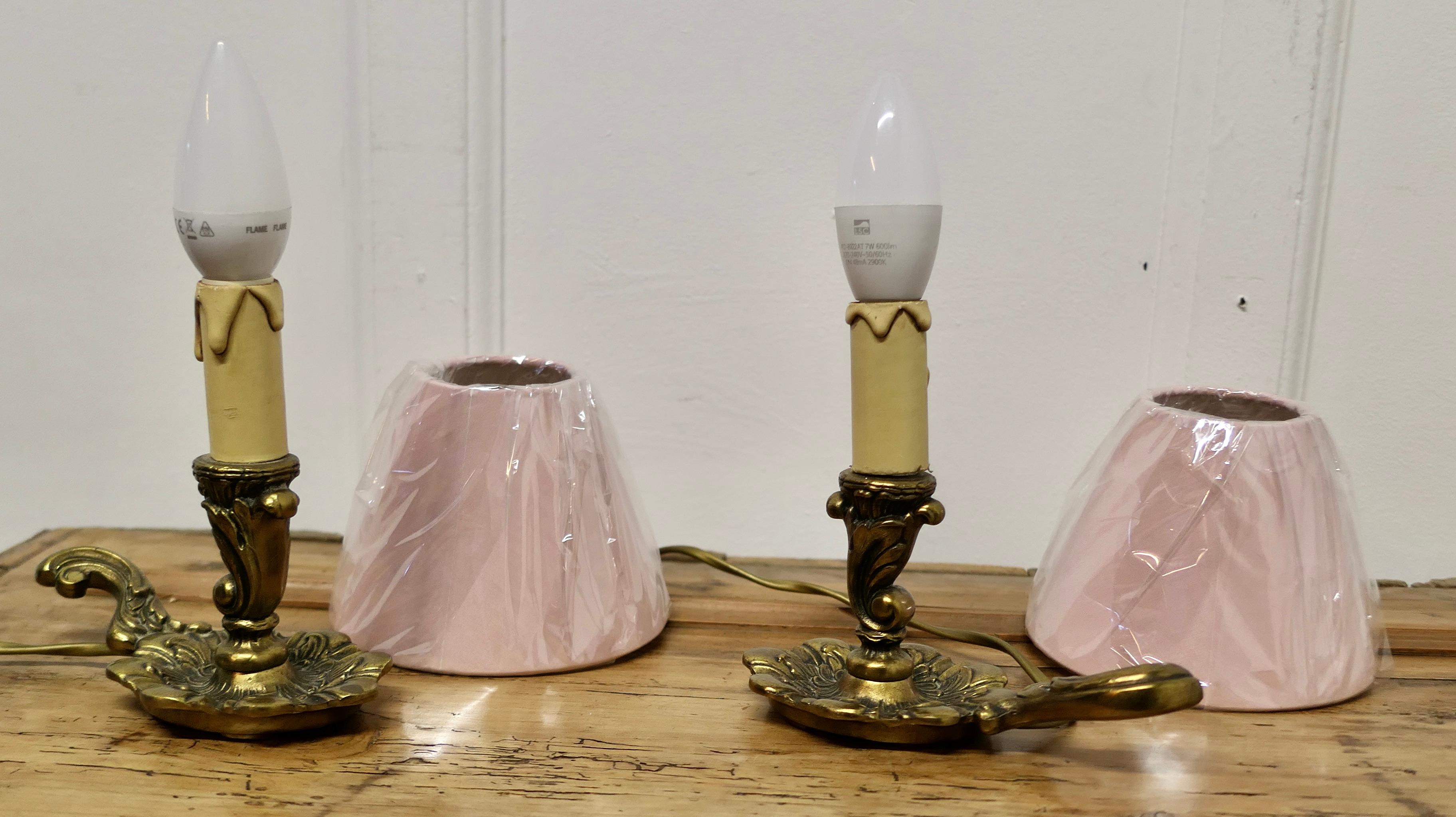 Pair of French Brass Bedside Lamps   

These are a good quality pair of small decorative bedside lamps, the bases are made in solid brass in the shape of a candlestick with a handle to one side
They have pretty new shades in pink
The lamps are good