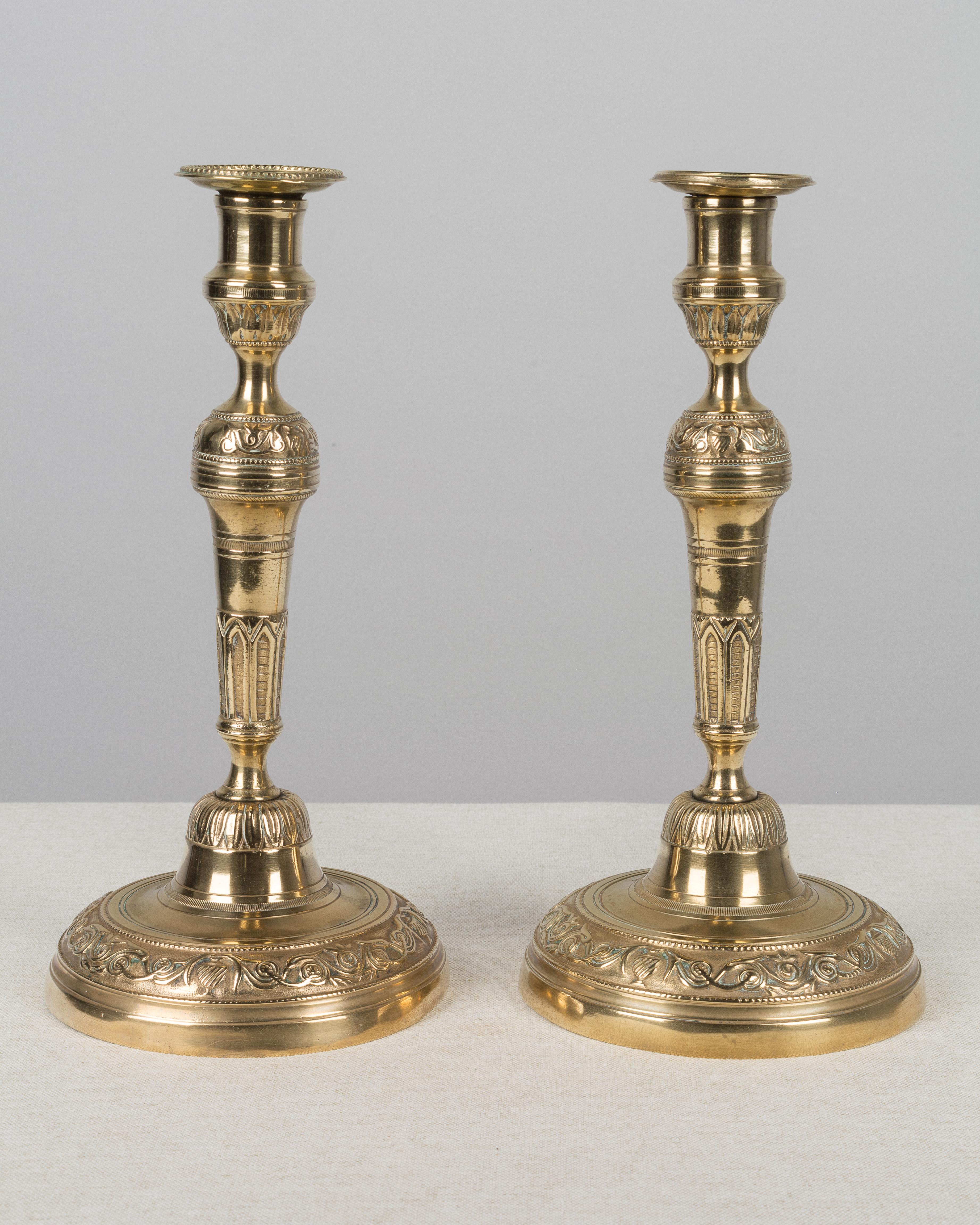 Pair of French Louis XVI style polished brass candlesticks. The bases are slightly dented. The bobeches are slightly different.