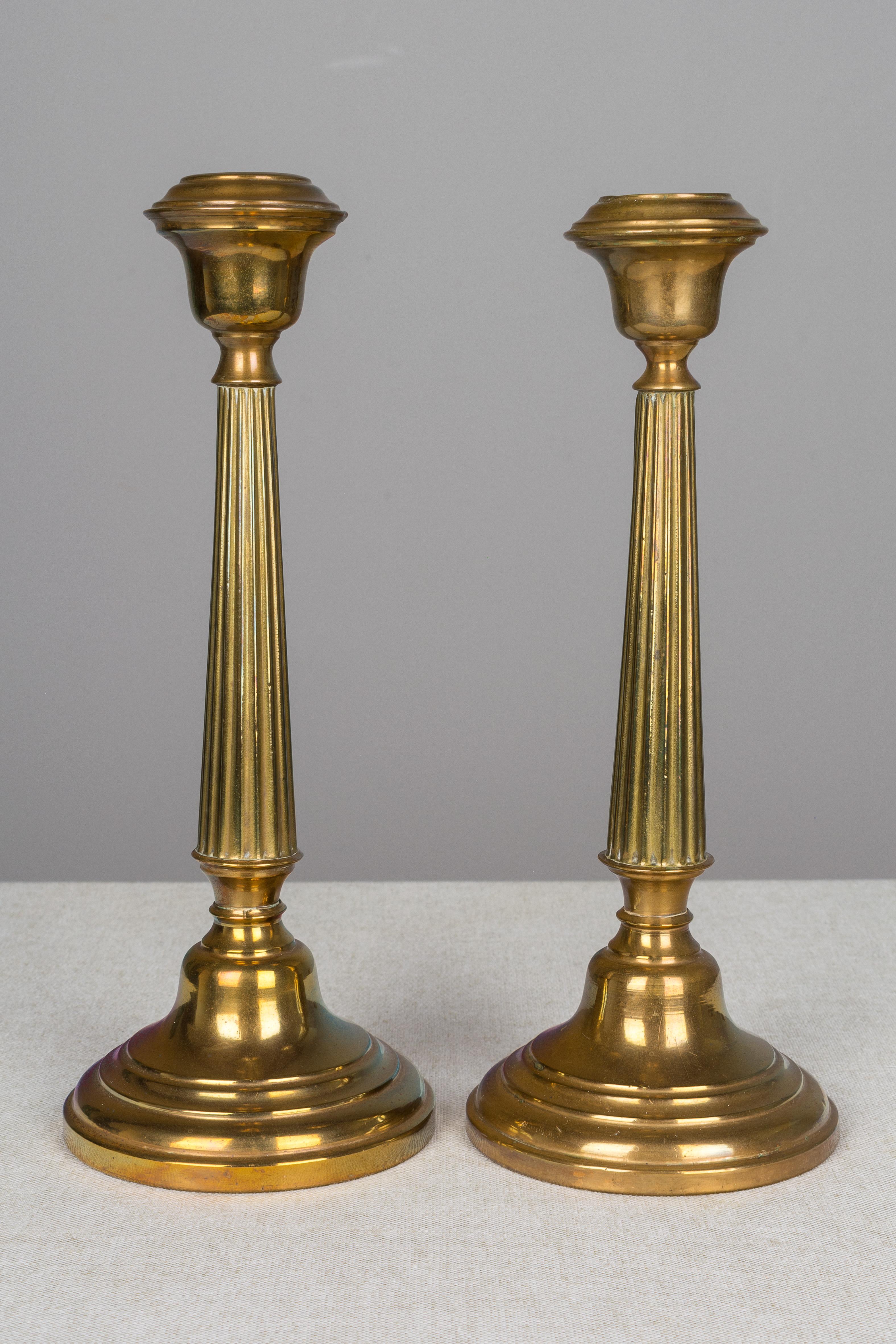 A pair of French brass candlesticks with simple reeded column body and warm patina.