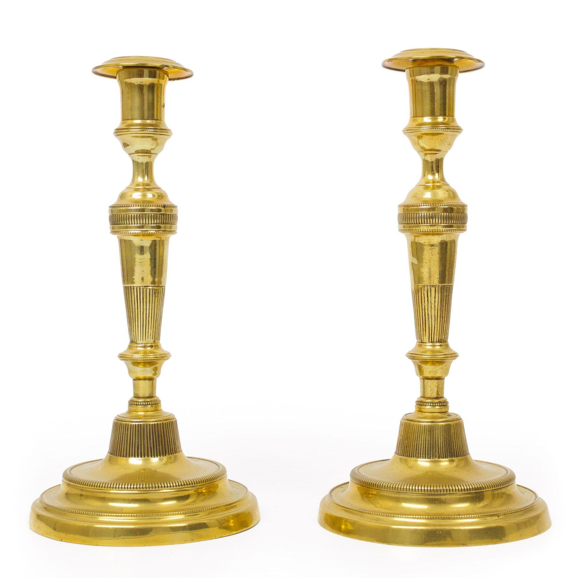 A good pair of Directoire period brass candlesticks circa the first quarter of the 19th century, they exhibit separately formed candle wells that remove from the stem over a ring-turned cup and tapered baluster with incised and pressed details over