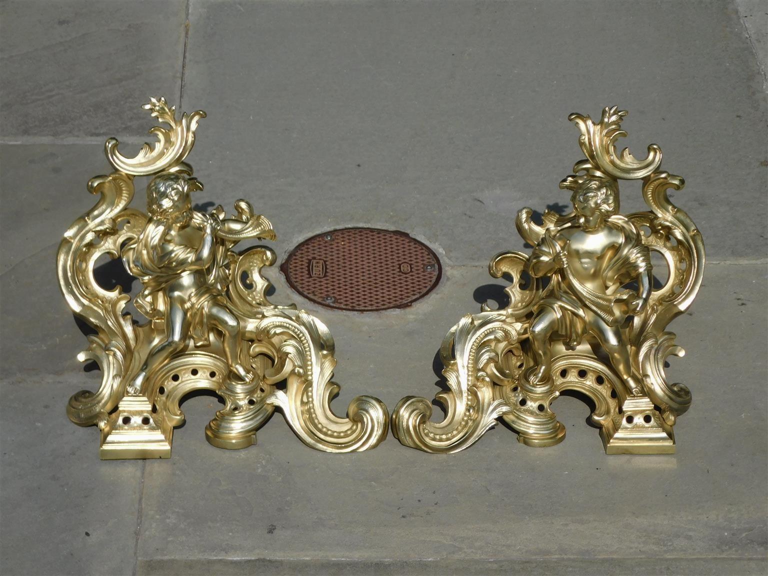 Pair of French brass flanking figural musical and foliage scrolled free standing fire place chenets, Early 19th Century.