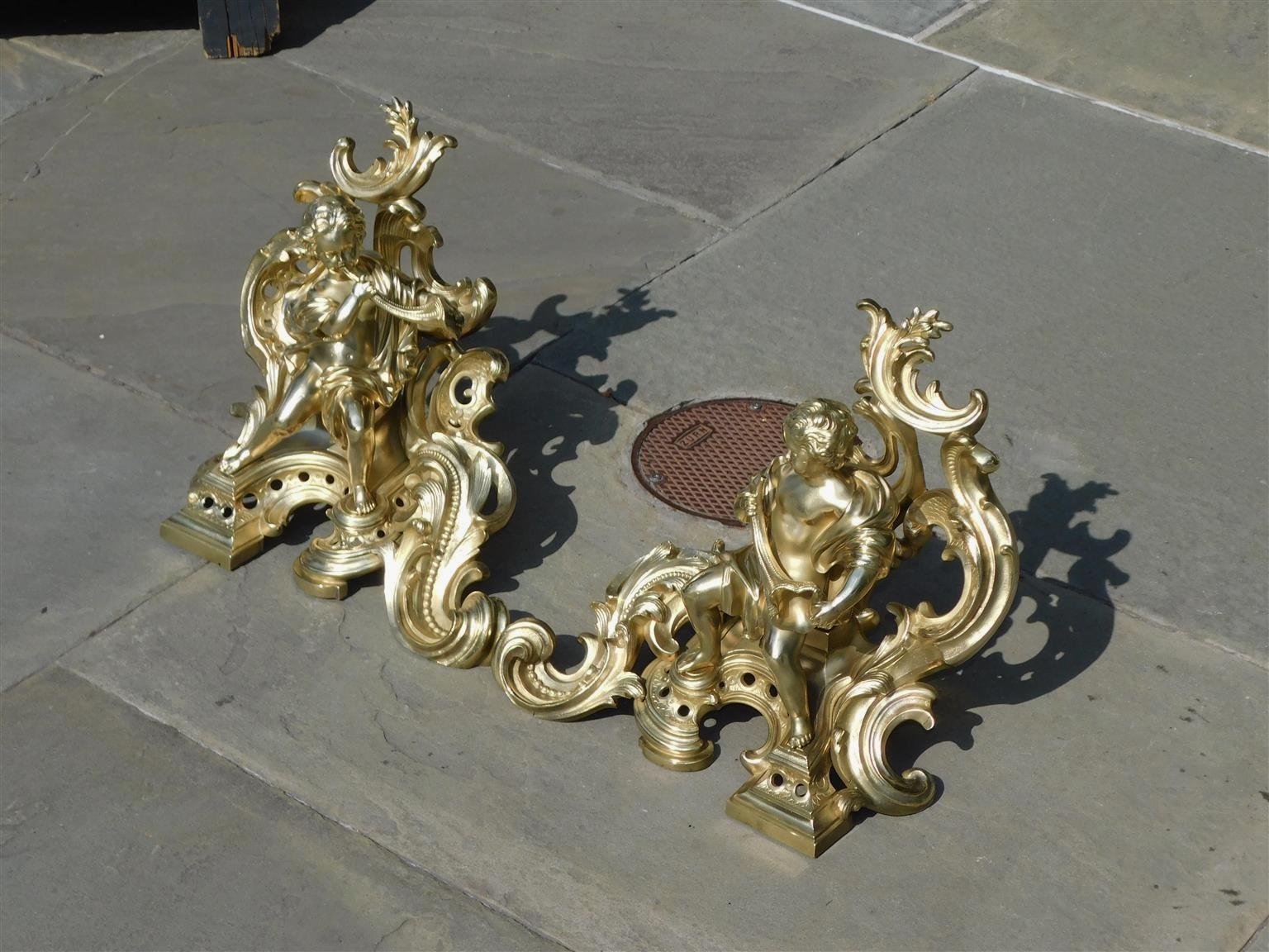 Cast Pair of French Brass Flanking Figural Musical & Foliage Scrolled Chenets, C 1810 For Sale