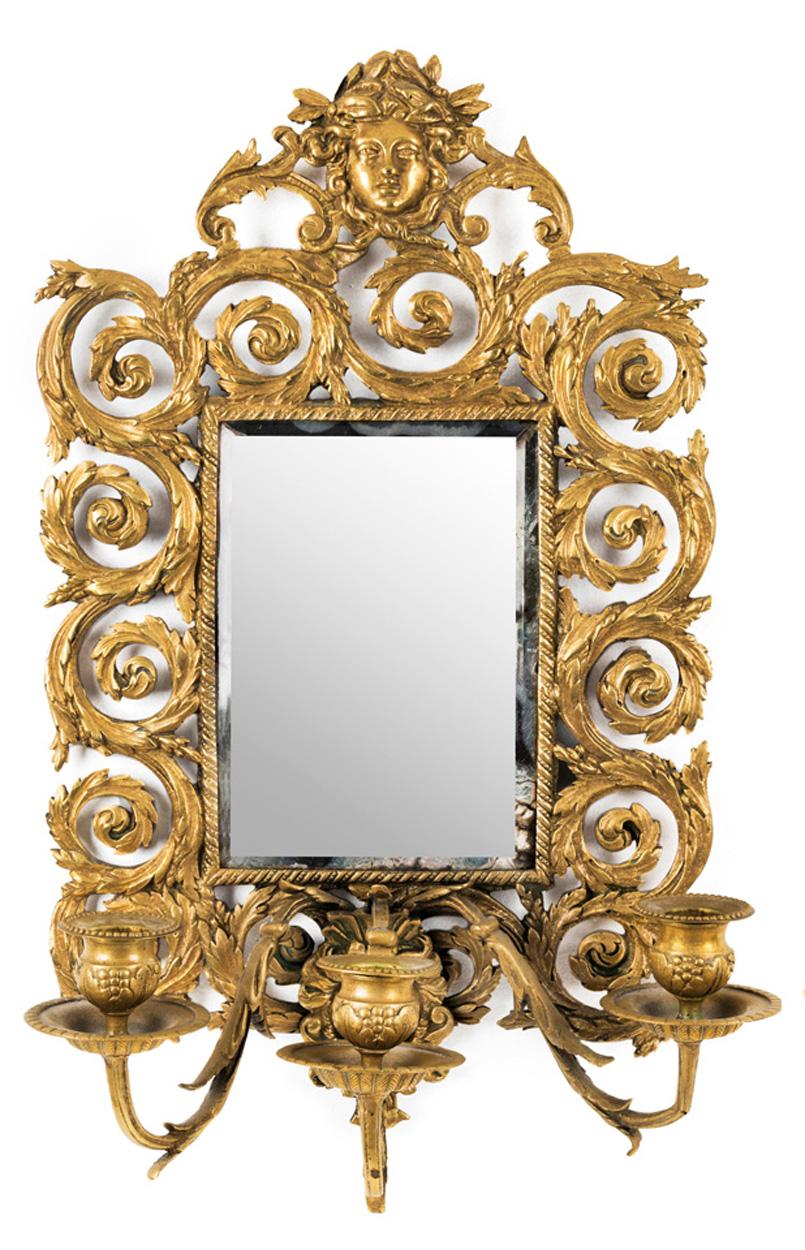An attractive pair of small baroque style brass girandole mirrors of fine quality. The decorative frames comprised of intertwined leafy scrolls surmounted by a sun maiden. Each mirror having three scrolled candle sconces and their original mirror