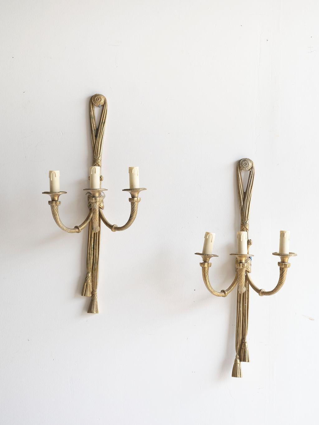 A lovely pair of French brass twisted wall sconces, in the style of Louis XVI, with three arms. Each arm has a candelabra holder with a plastic fake candle on it. The fake candle has fake 