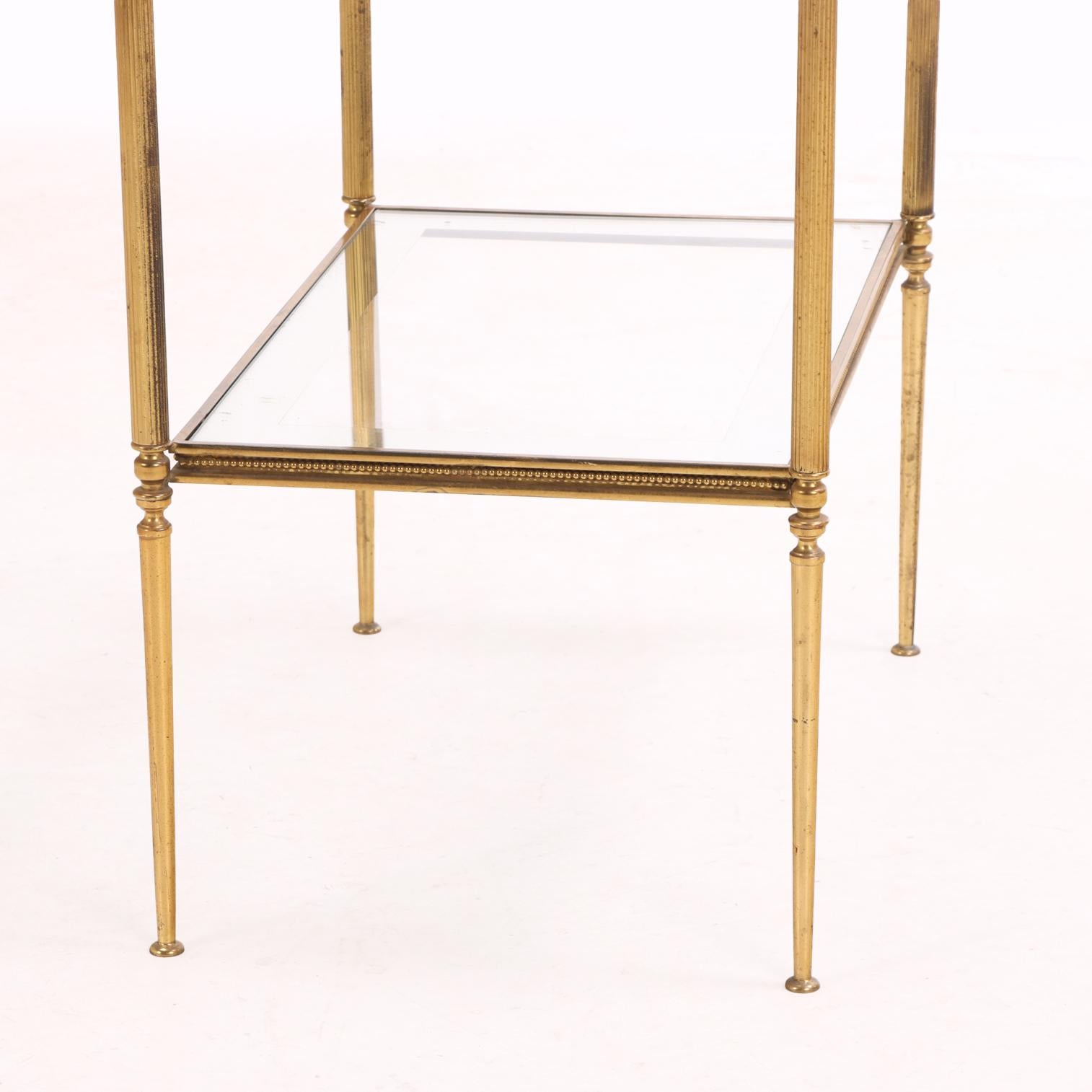 Each table features a brass frame with two glass shelves edged in a silvered border. Elegant storage and versatile, they offer mid-century sophistication and are ideal as side or cocktail tables.